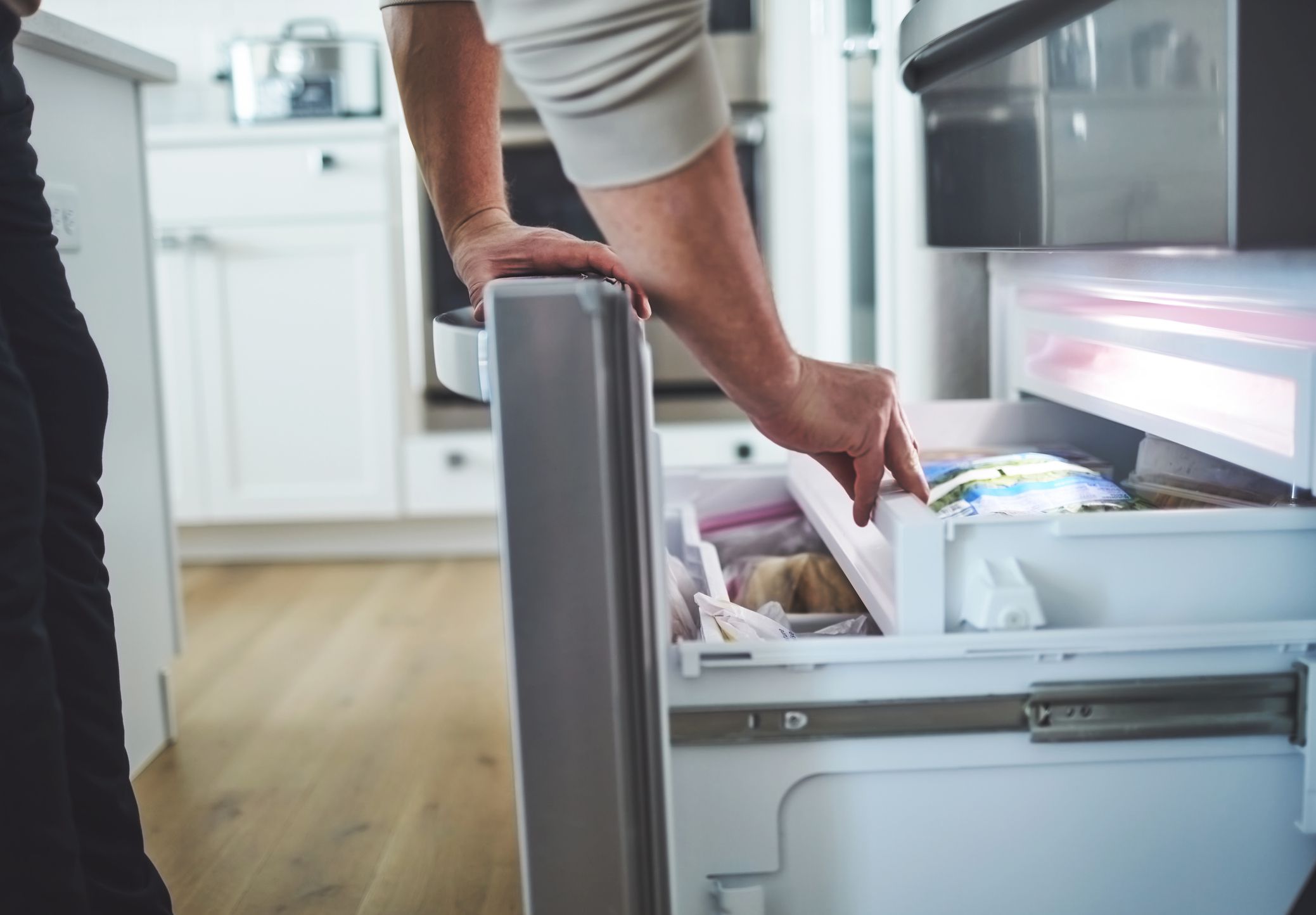 Unidentifiable male looking in an opened freezer drawer of a refrigerator