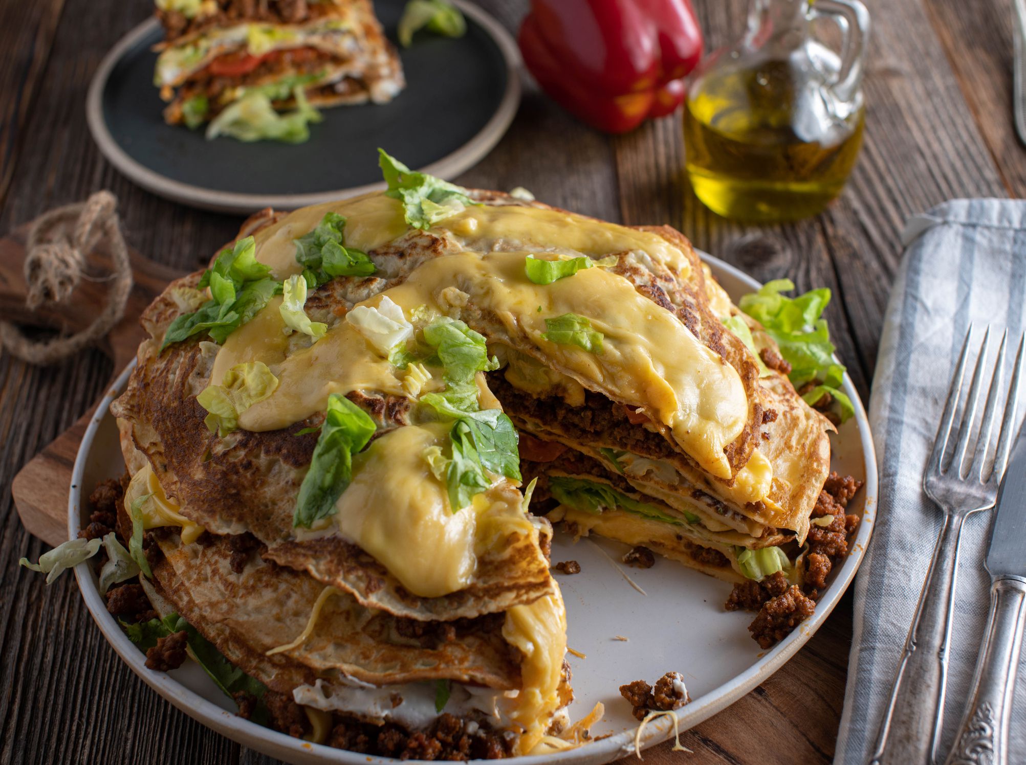 Delicious savory pie made with pancakes filled with ground beef, beans, sour cream, tomatoes, lettuce and cheese. Served on rustic and wooden table background. Ready to eat