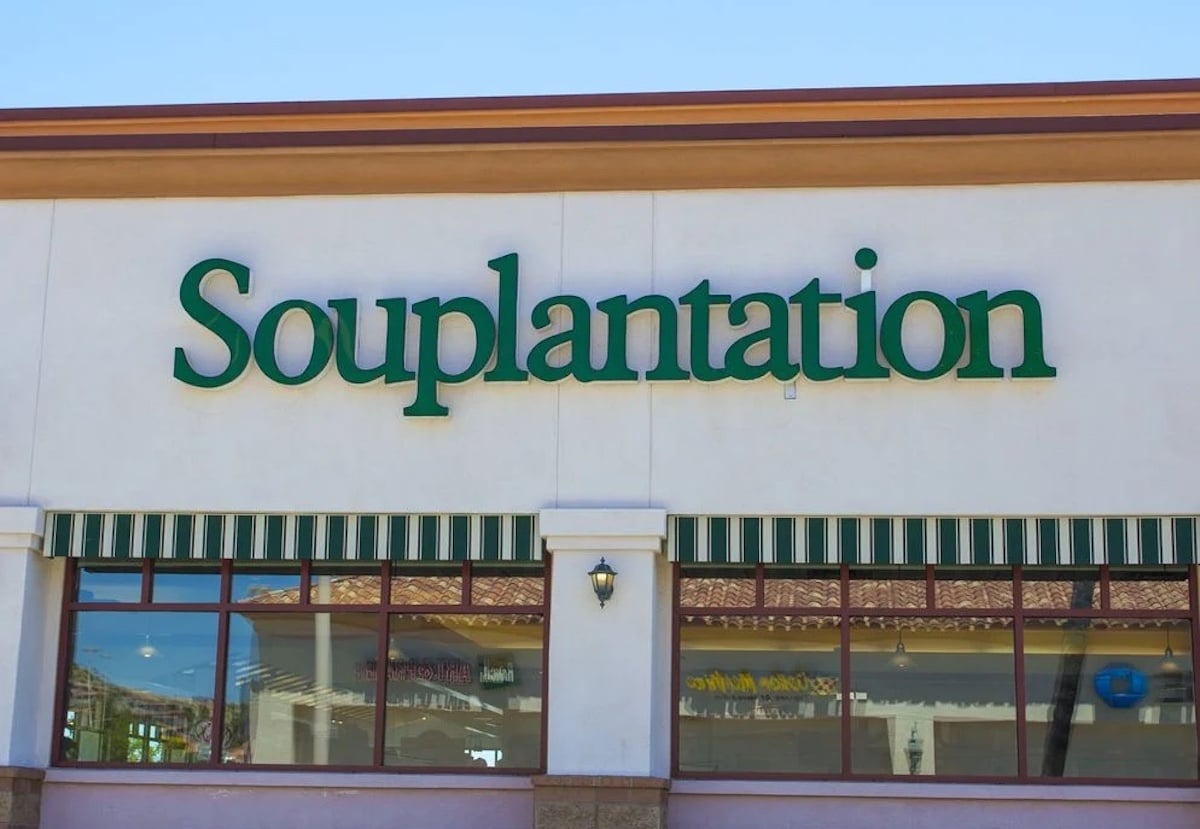 The exterior of a Souplantation restaurant, one of the beloved old restaurant chains, features its green logo sign on a white wall above striped green-and-white awnings and large windows.