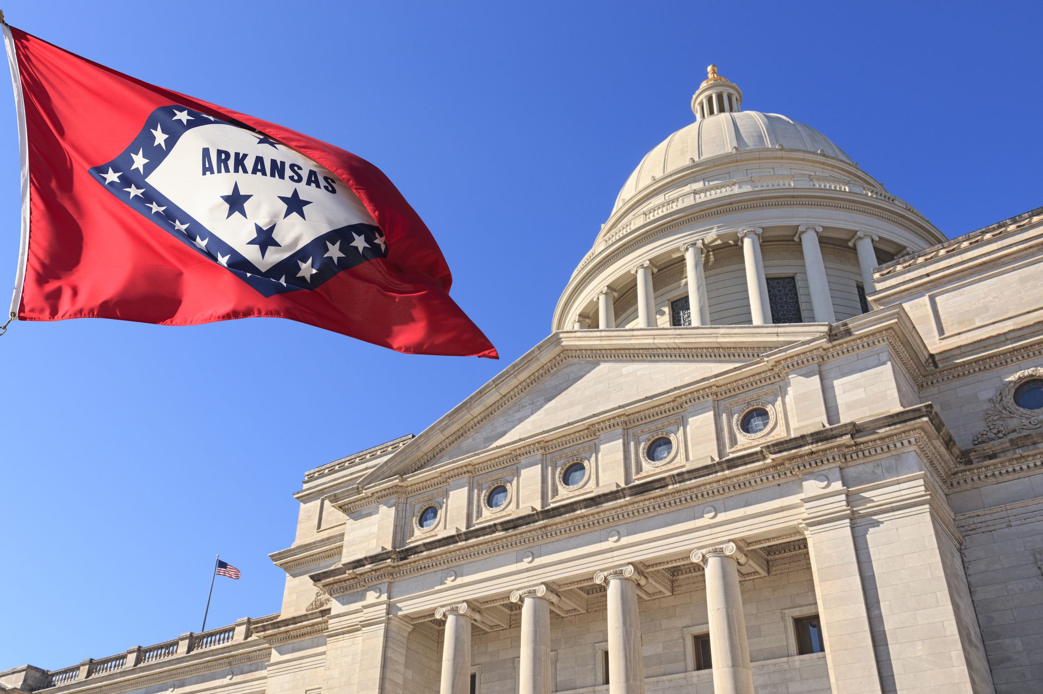 State Capitol Building front exterior in Little Rock Arkansas with US state flag outside on clear windy day with blue sky.