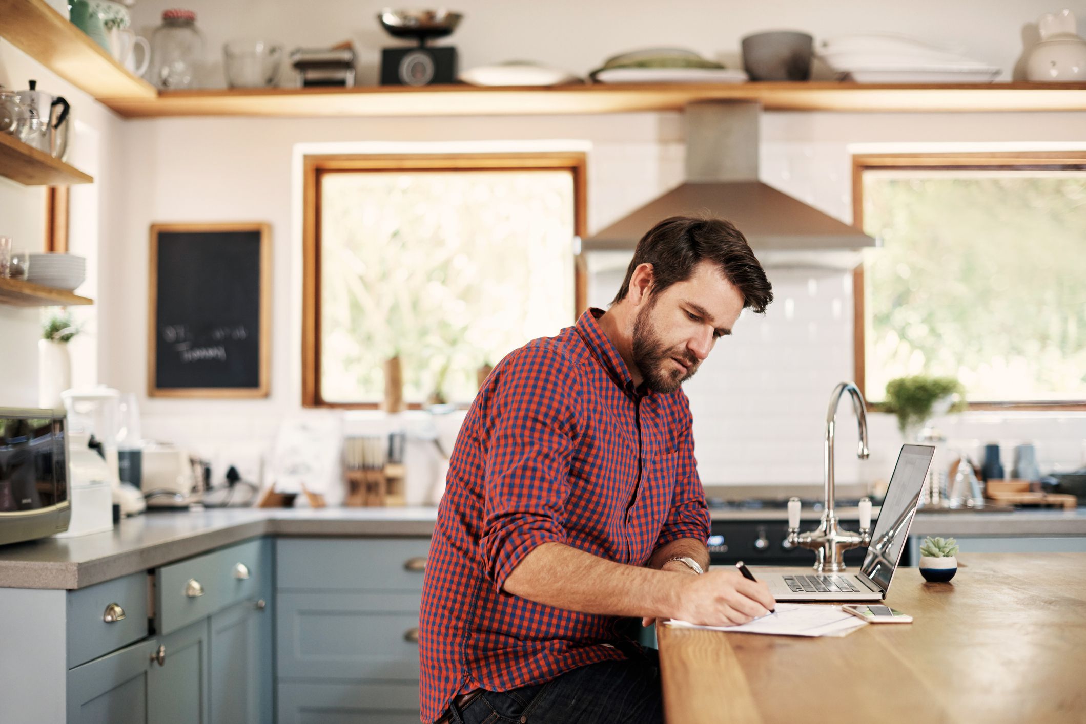 Shot of a handsome man sitting at his kitchen counter with his laptop