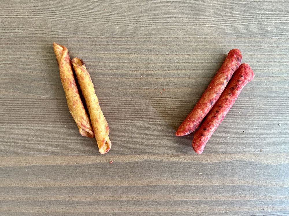Two pairs of rolled snacks are placed on a wooden surface, with a yellowish pair on the left and a reddish pair on the right.