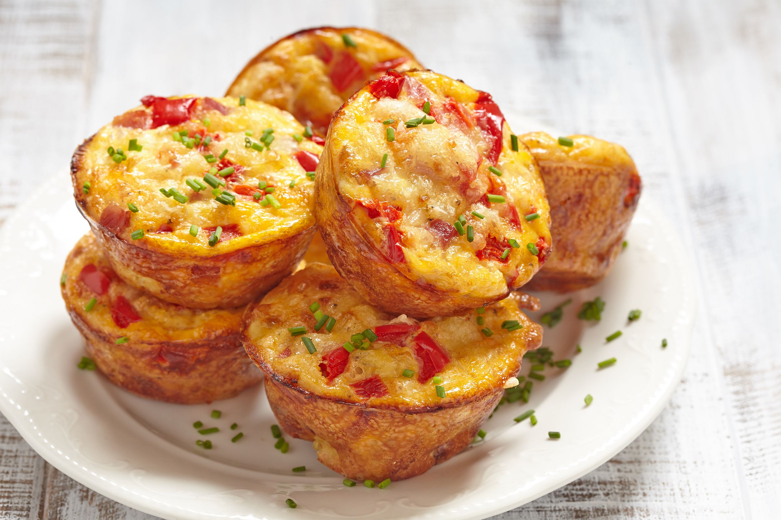 A pile of egg muffins on a white plate on a rustic white wooden table