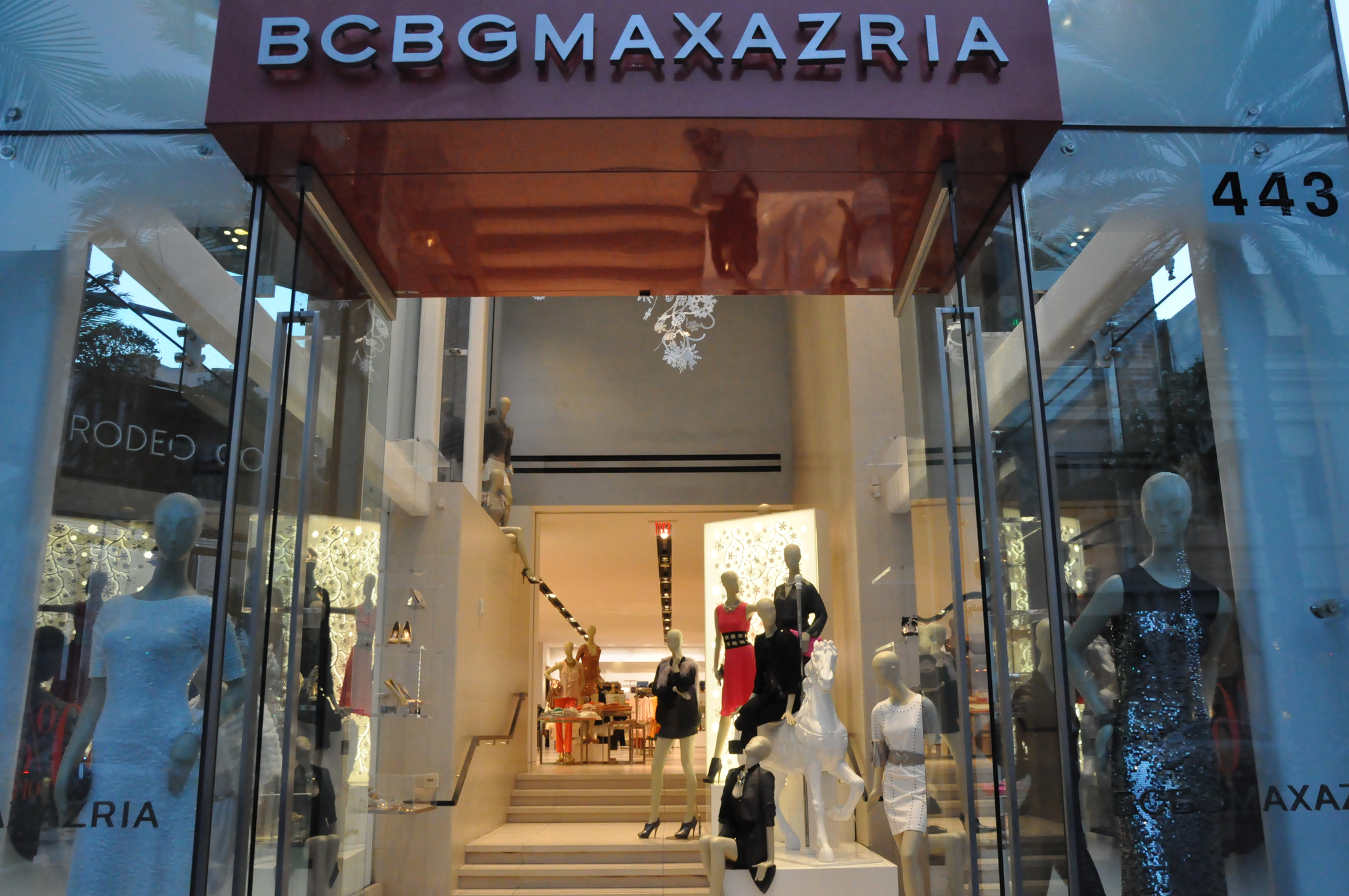 Opened doors showcasing interior of BCBGMAXAZRIA store on Rodeo Drive, Beverly Hills, California, numerous mannequins wearing clothing from the store, very well-lit and flashy store