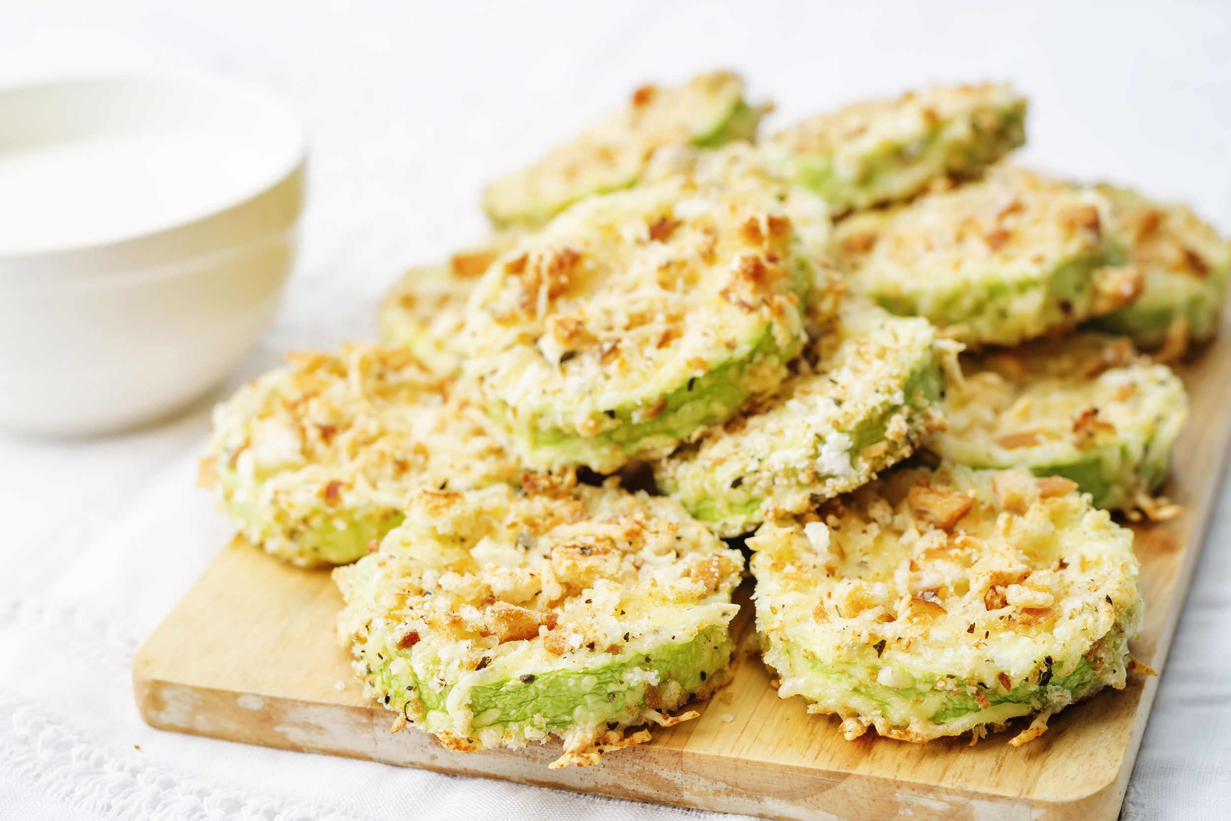 Baked parmesan zucchini crisps on a wooden cutting board on a white tablecloth with a blurred background