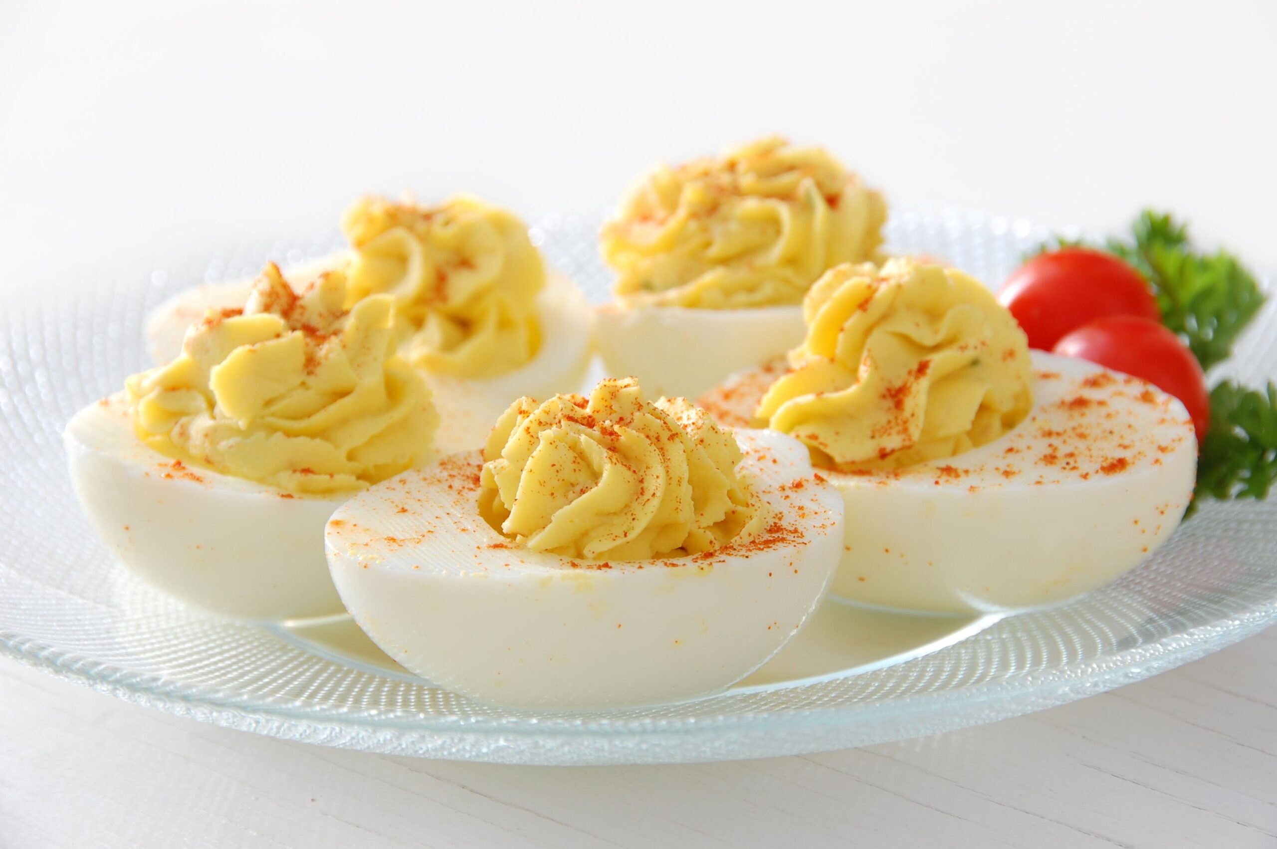 Closeup of five healthy deviled eggs in a circle on a decorative glass plate with garnish on a white table