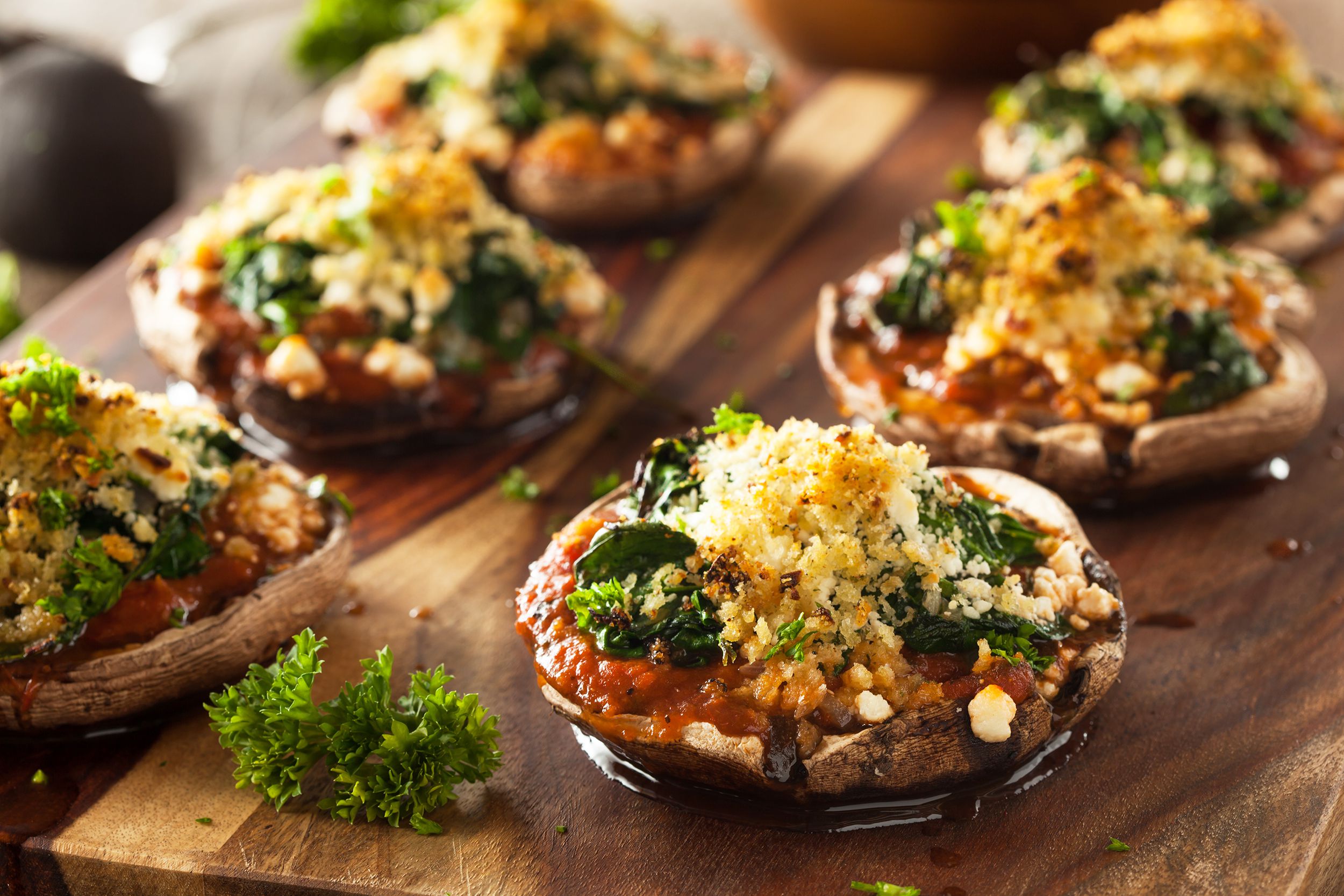 Closeup of homemade baked stuffed Portobello mushrooms with spinach and cheese on a wooden cutting board blurred in the background