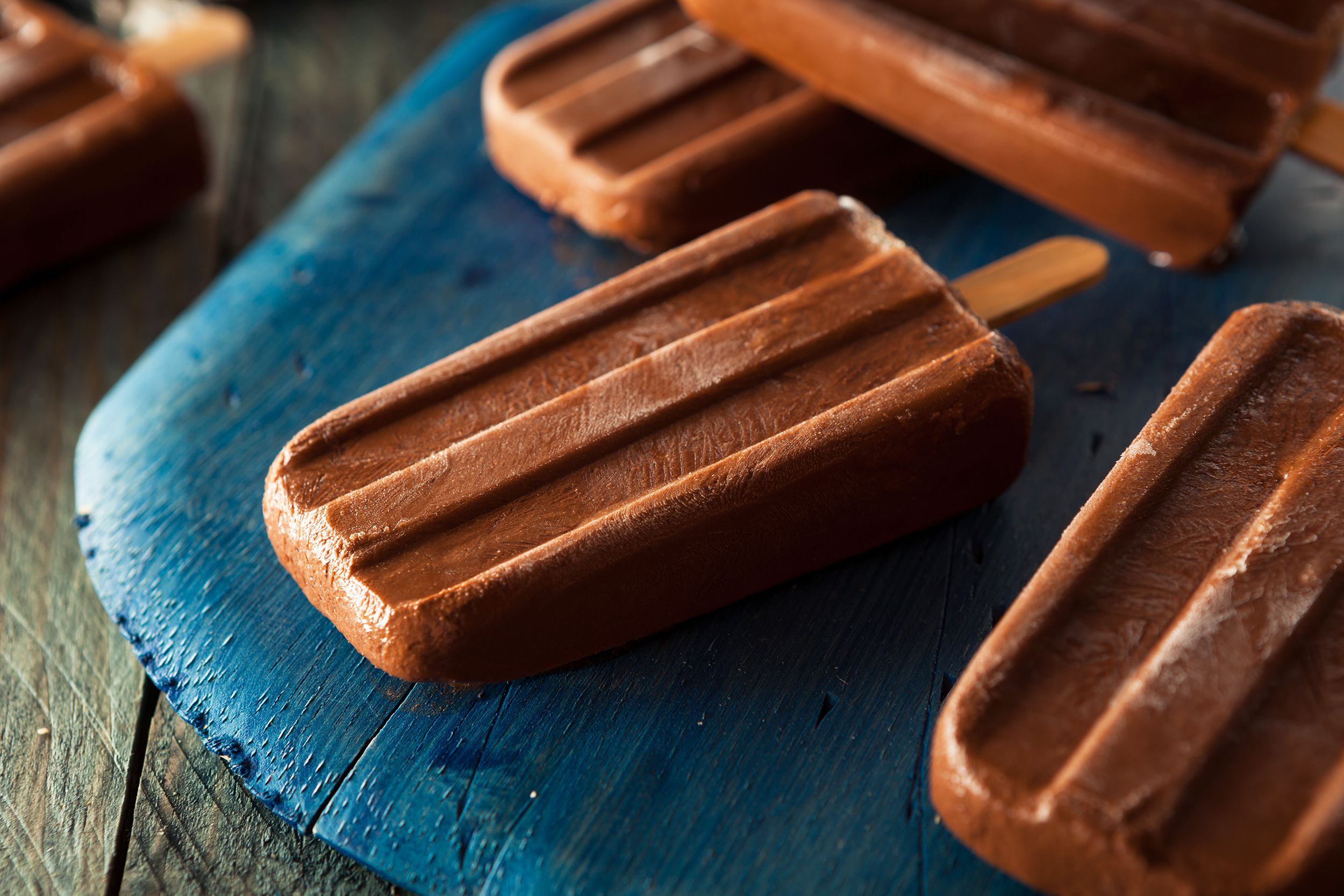 Closeup of four mocha ice pops on a blue wooden cutting board on a wooden table with a blurred background