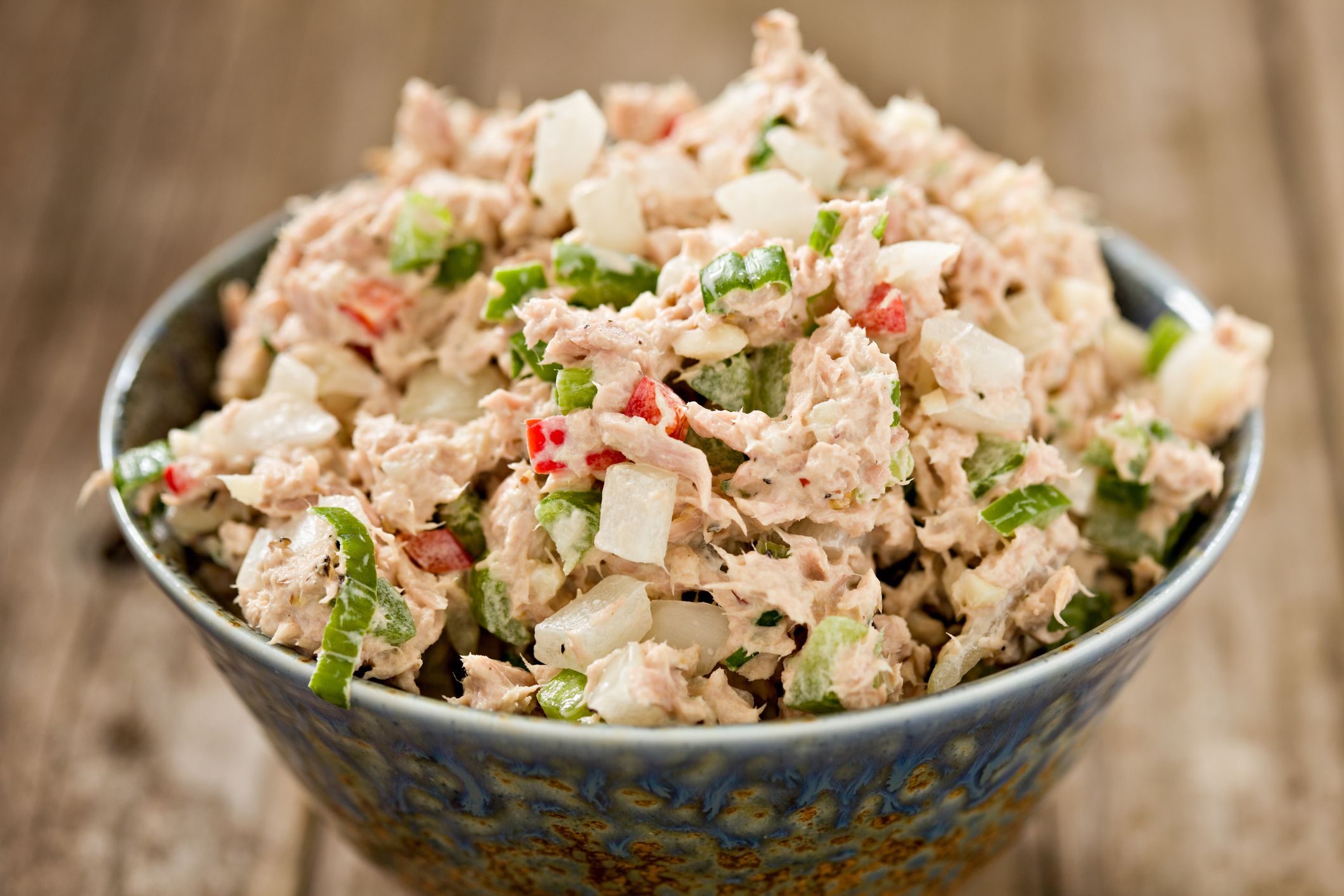 Closeup of Greek yogurt tuna salad in a blue and brown ceramic bowl with a blurred background of a rustic wooden table