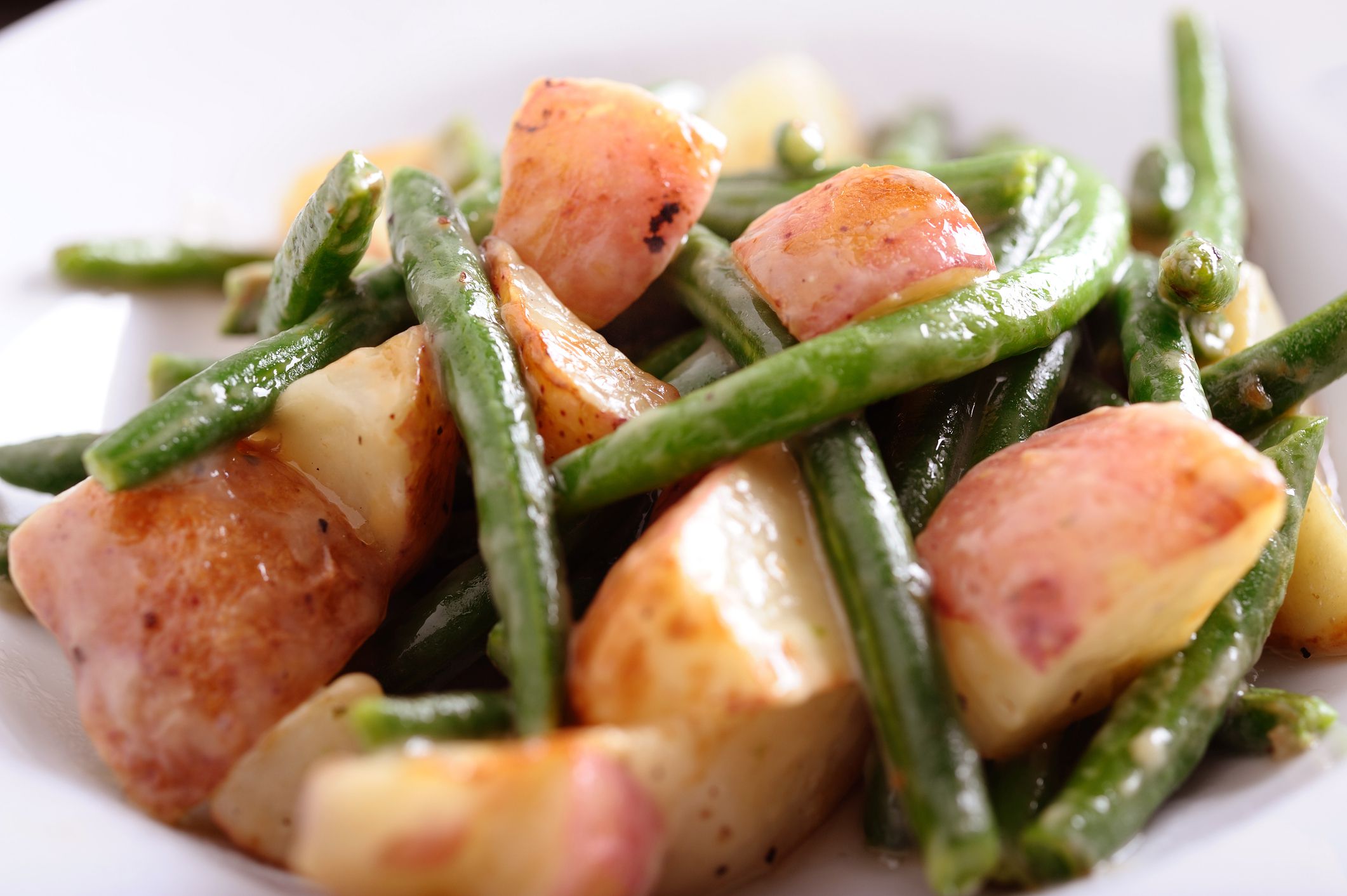 Closeup of green beans and potatoes in chunky tomato sauce in a white bowl