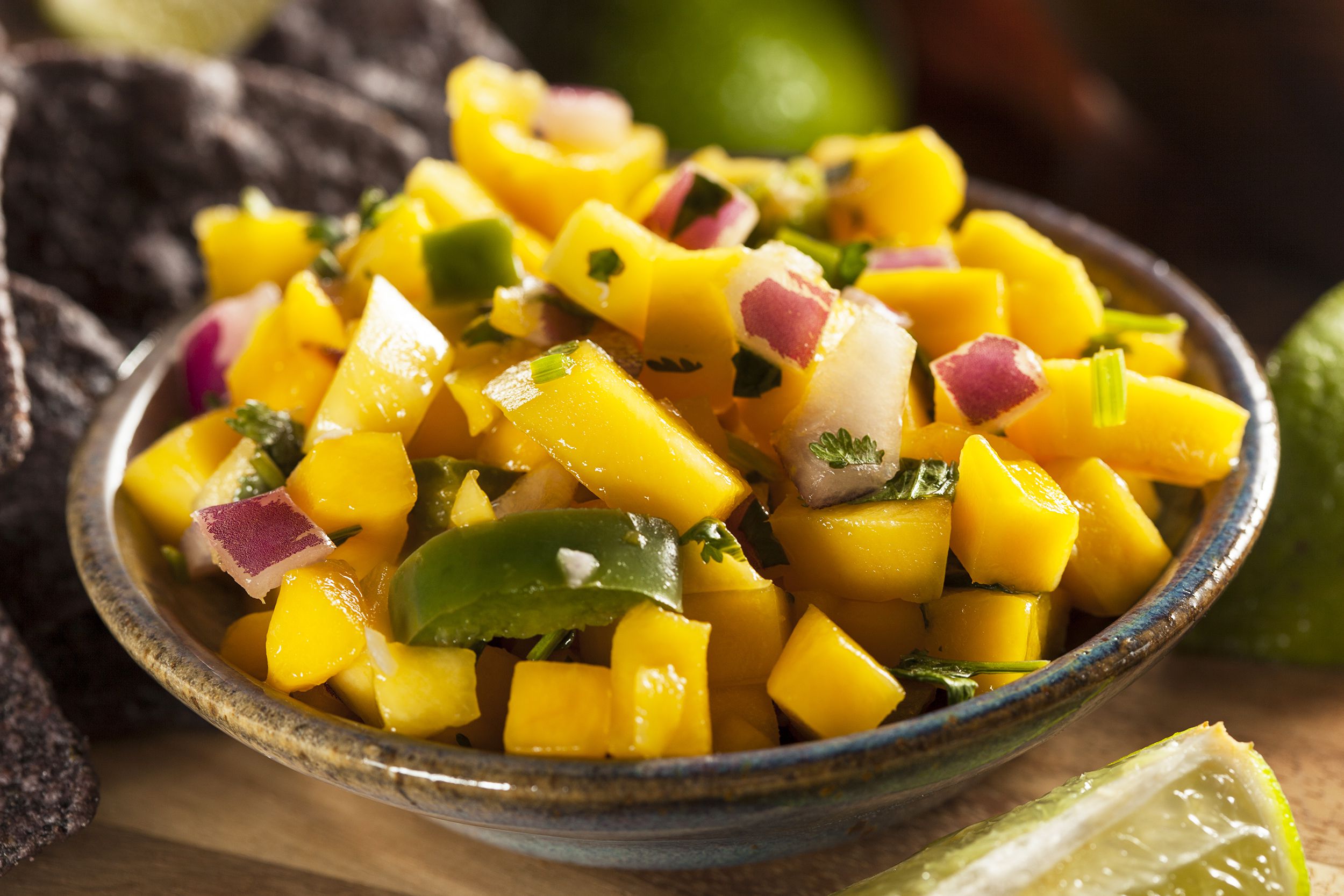 Closeup of homemade corn & mango salad in a ceramic brown bowl with a blurred background of ingredients