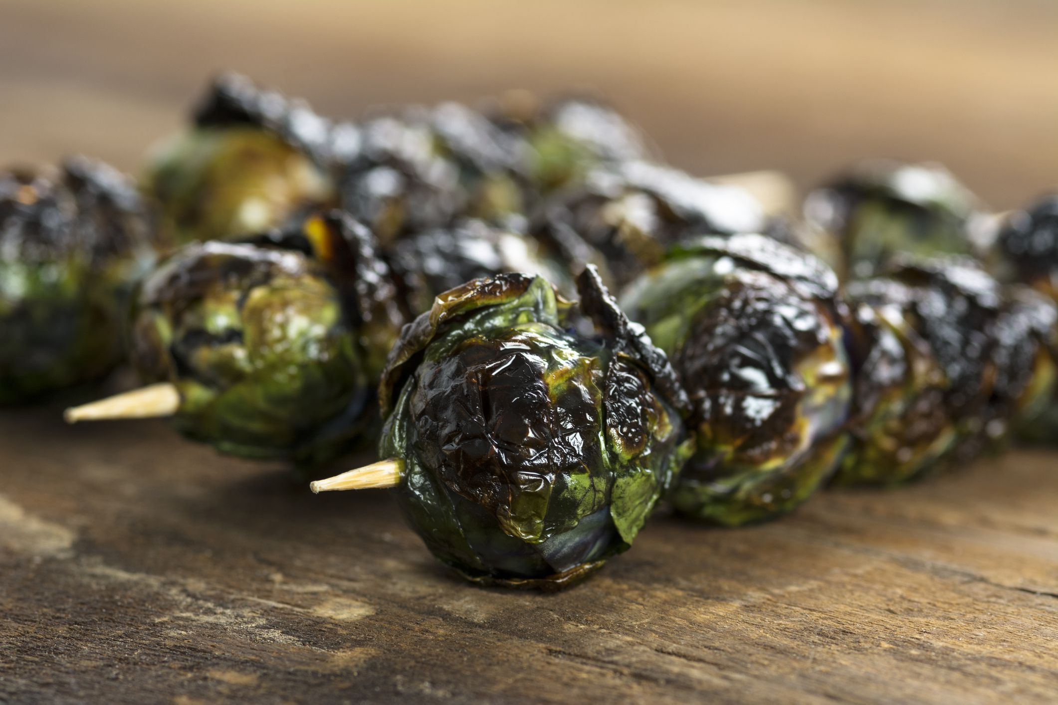 Closeup of three bacon brussels sprout skewers on a wooden board