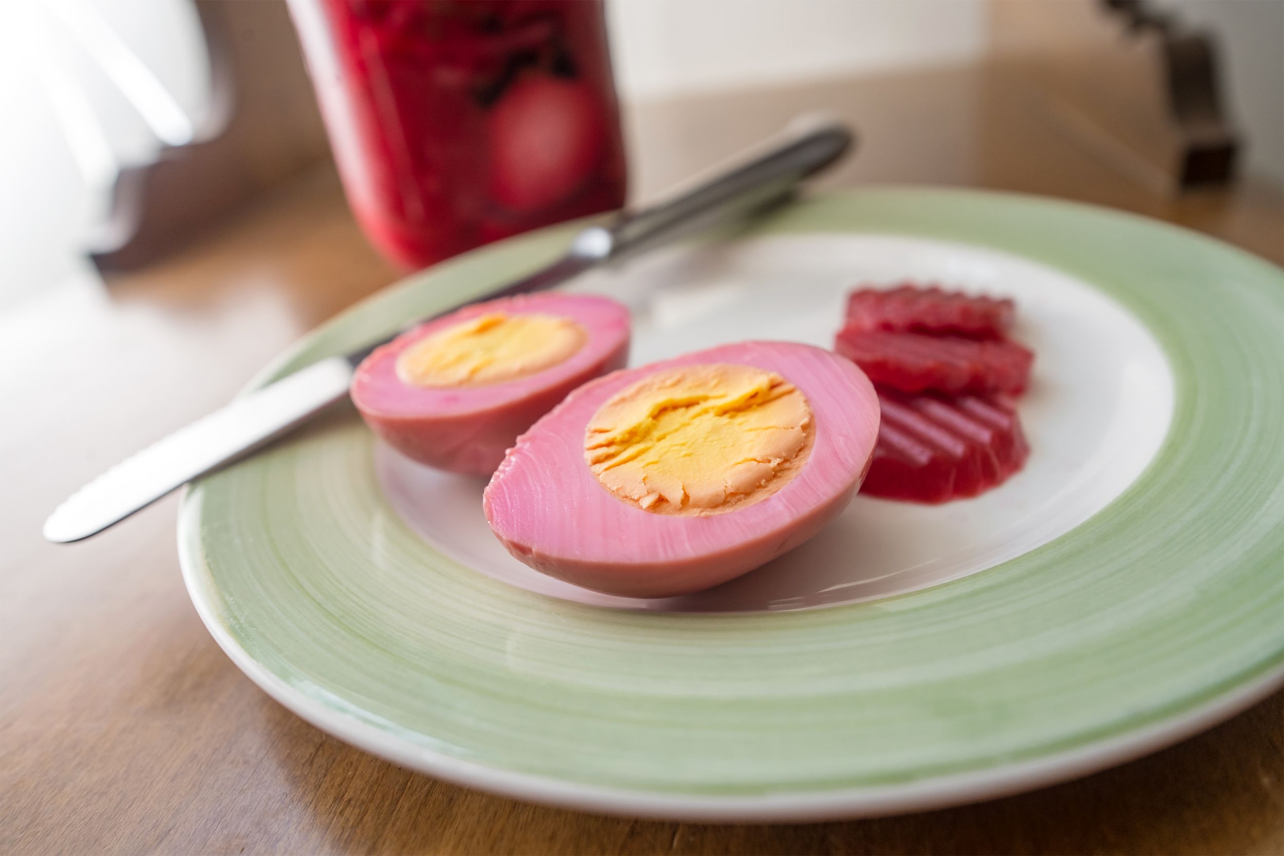Focus on a jalapeno pickled egg cut in half on a sage green plate with a knife on a wooden table with a blurred background