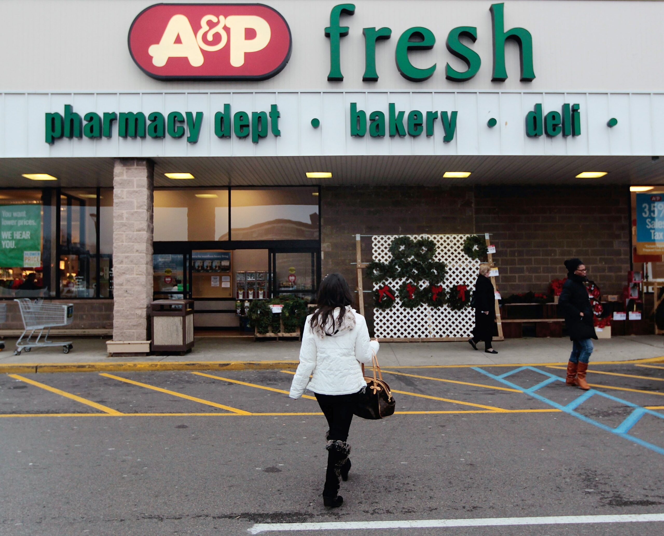 Front exterior of A&P grocery store, Jersey City, New Jersey, front doors and a few shopping carts, one woman walking towards store in the drive-through road