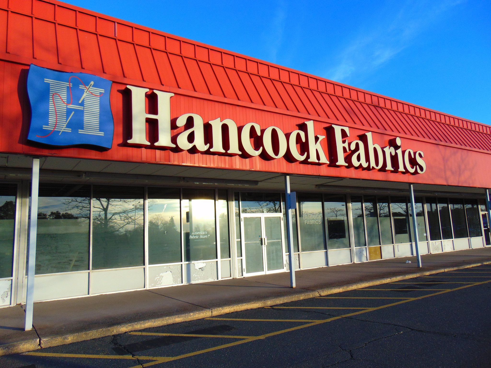 Front exterior of closed Hancock Fabrics, Manchester, Connecticut, windows covered with paper, empty, road in the foreground and blue sky in the background