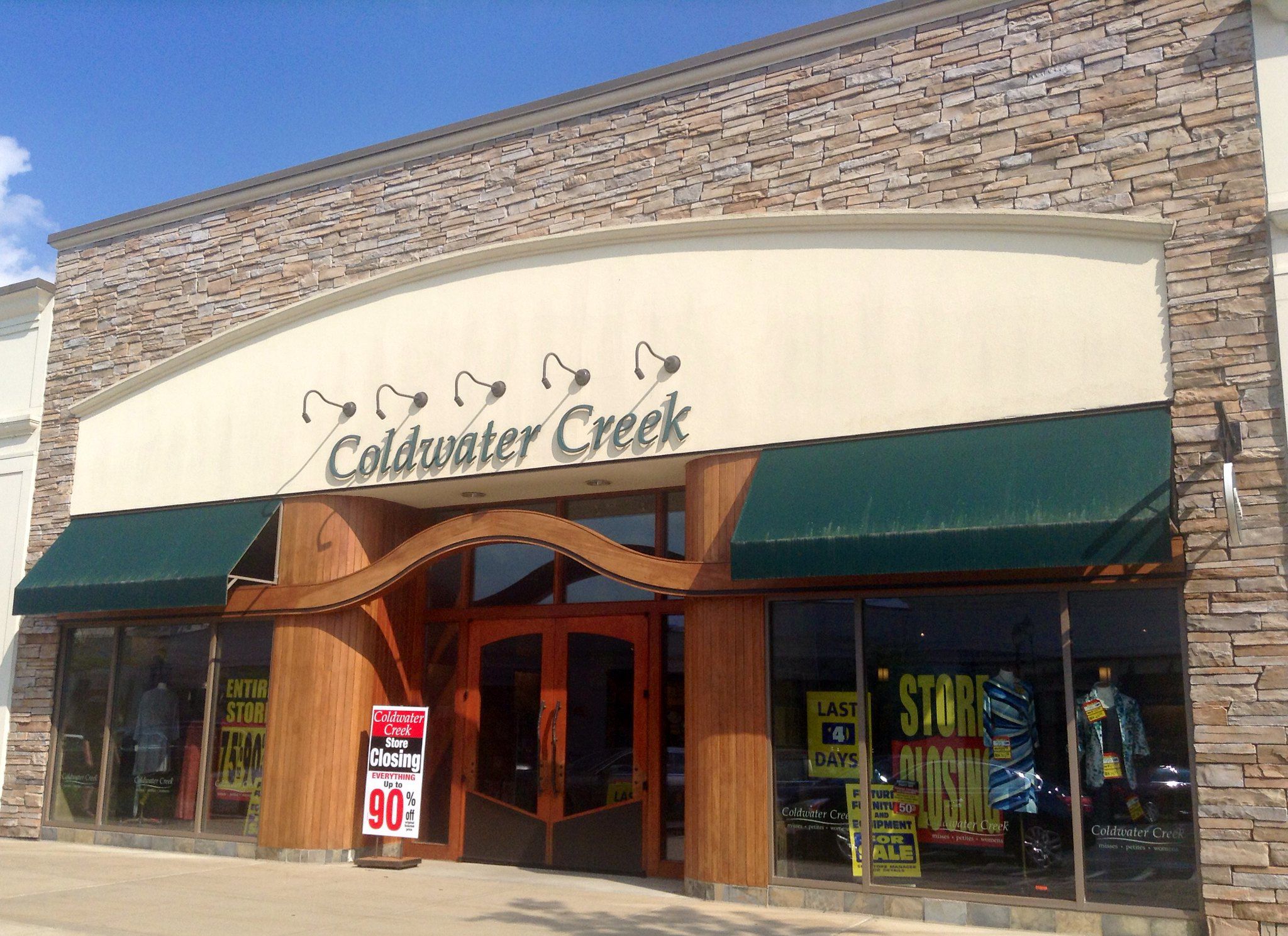 Front exterior of Coldwater Creek store, Manchester, Connecticut with a store closing sign in the front on the sidewalk and numerous store closing signs in the windows, on a sunny day, with a blue sky