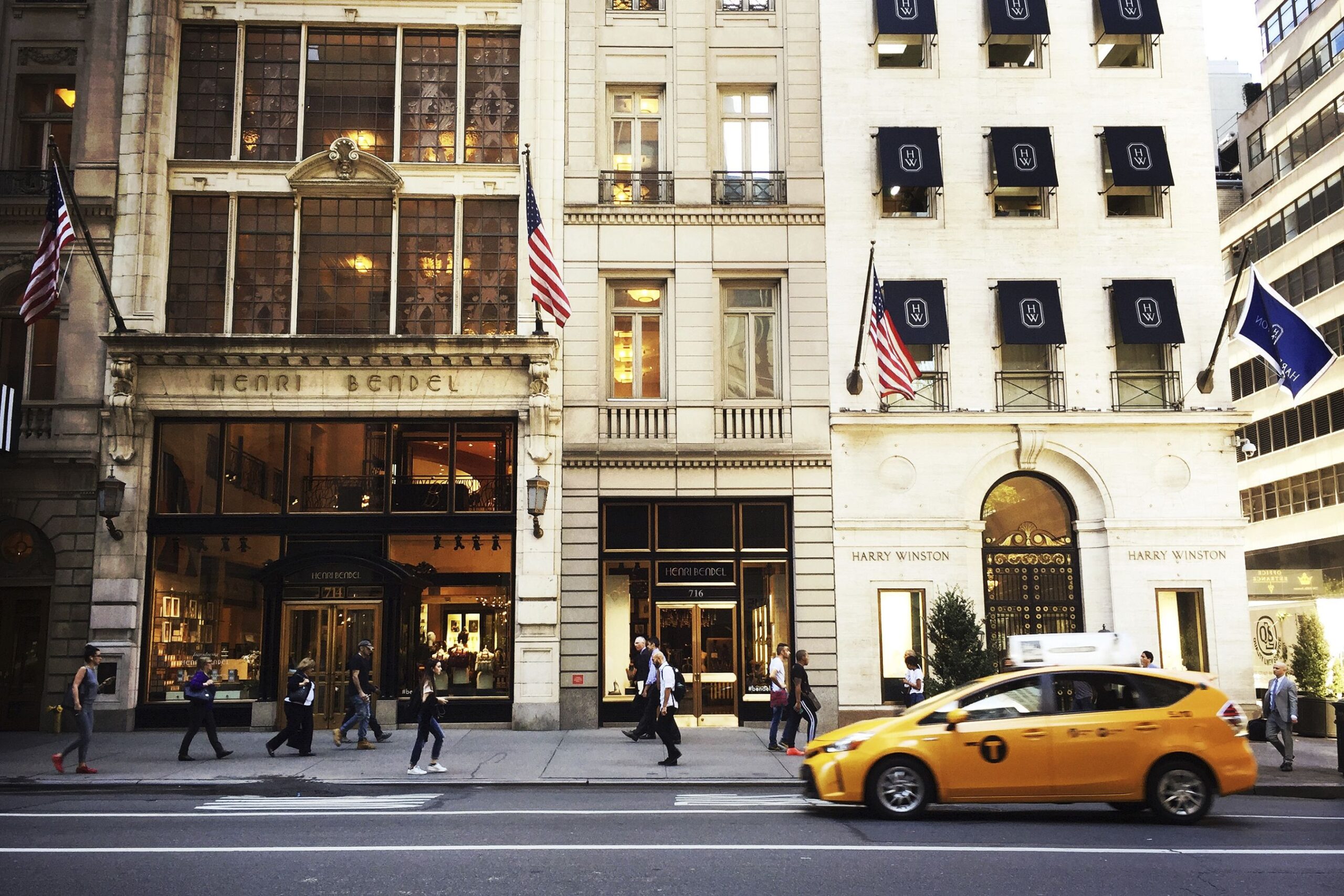 Front exterior of Henri Bendel store, Manhattan, New York City, next to a Harry Winston store, people walking along the sidewalk and one yellow taxi cab