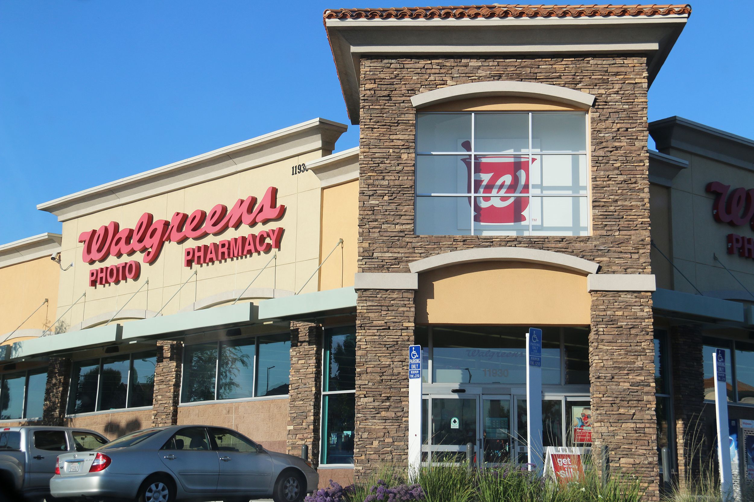 Front exterior of a Walgreens Pharmacy, Los Angeles, windows and front doors with a few cars parked on the left, on a sunny day with a clear blue sky