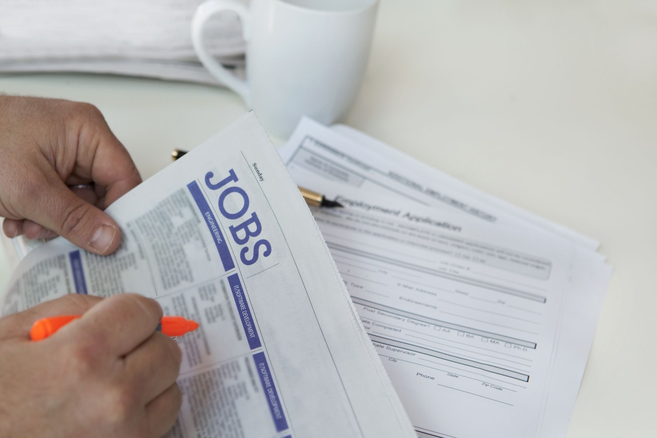 hands circling jobs in paper, unemployment papers in background