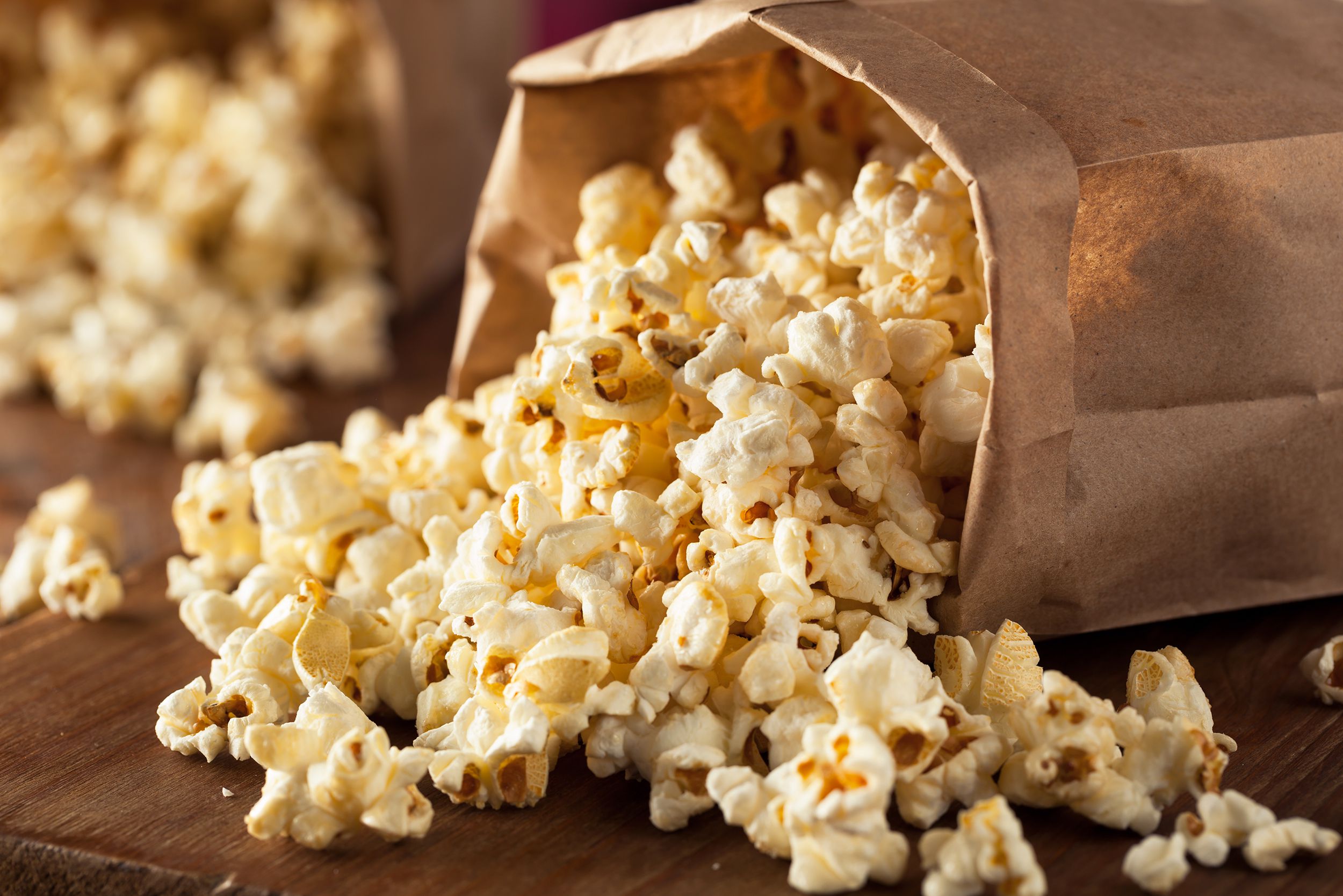Homemade kettle corn popcorn coming out of a bag on a wooden table with a blurred background of another another bag of popcorn coming out of the bag