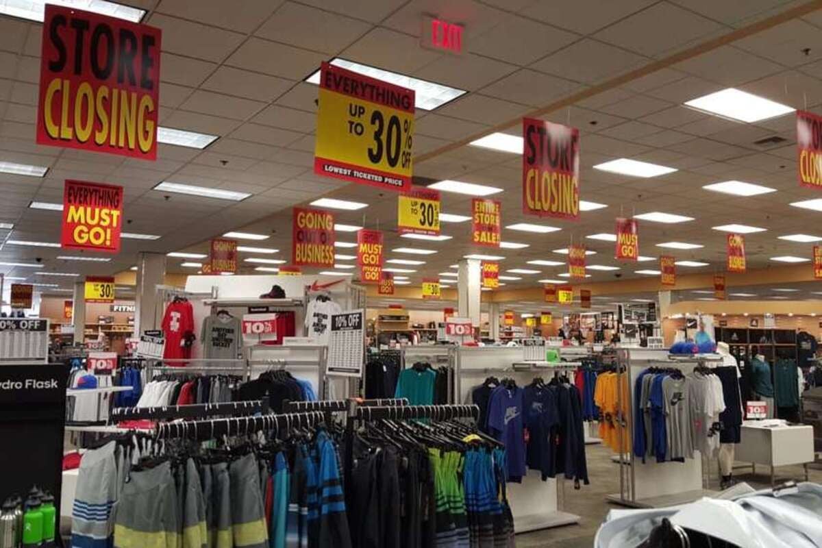 Interior of Sport Chalet, Burbank, California, several racks of mens' athletic clothes with numerous store closing sale signs hung from the ceiling, very well-lit, organized, and clean