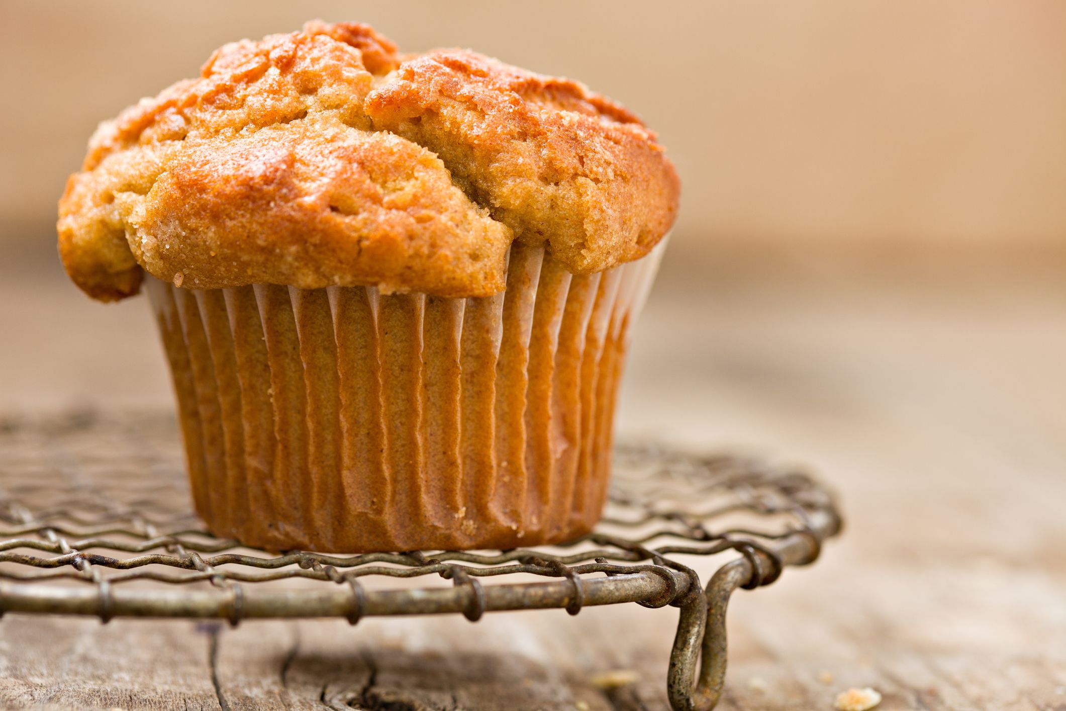 One mini pumpkin butterscotch muffin on a round baking wire pan on a wooden table with a blurred background