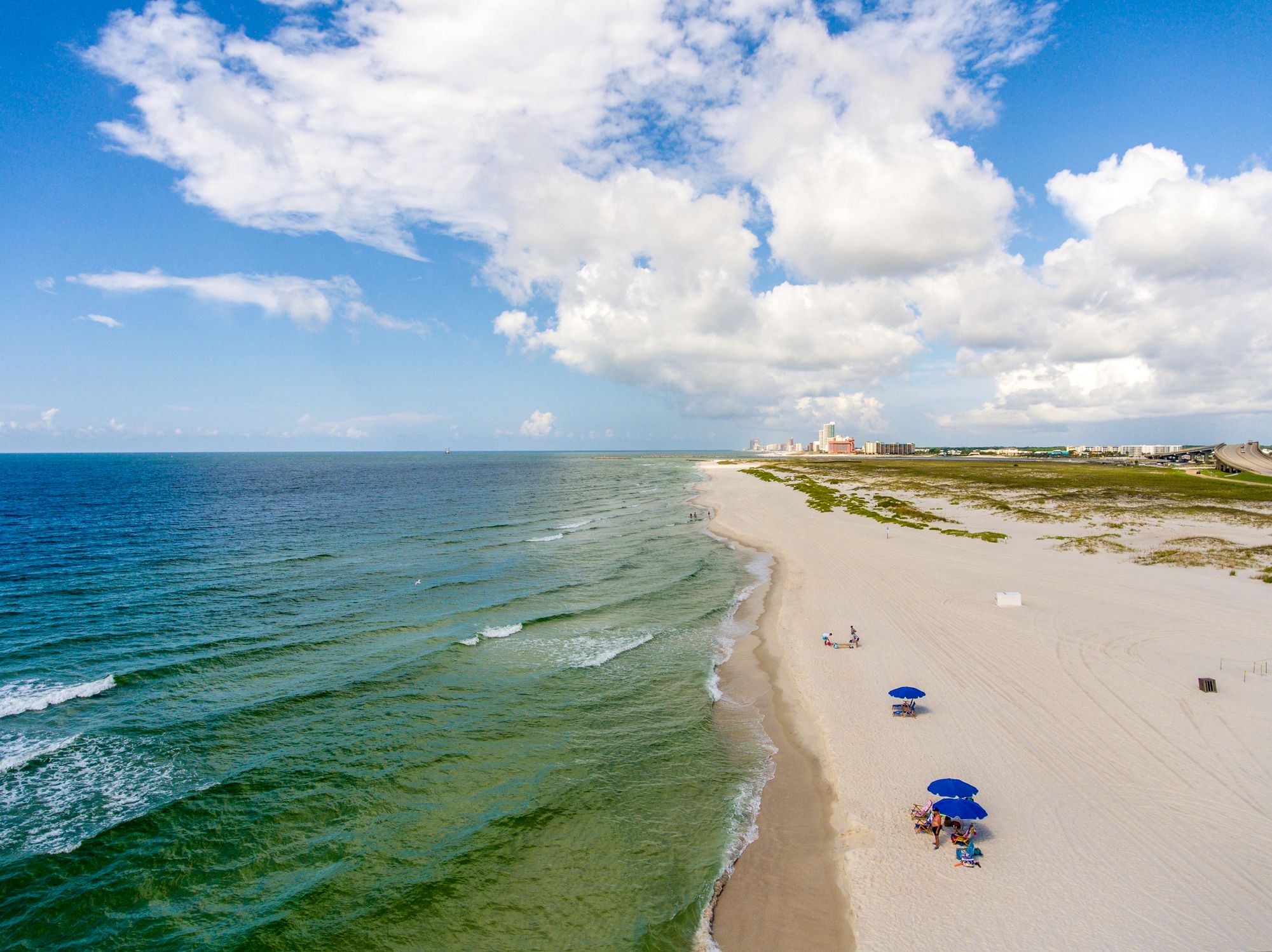 Orange Beach, Gulf Shores, Alabama during summer with a few people on beach, focus on ocean and blue sky with white clouds