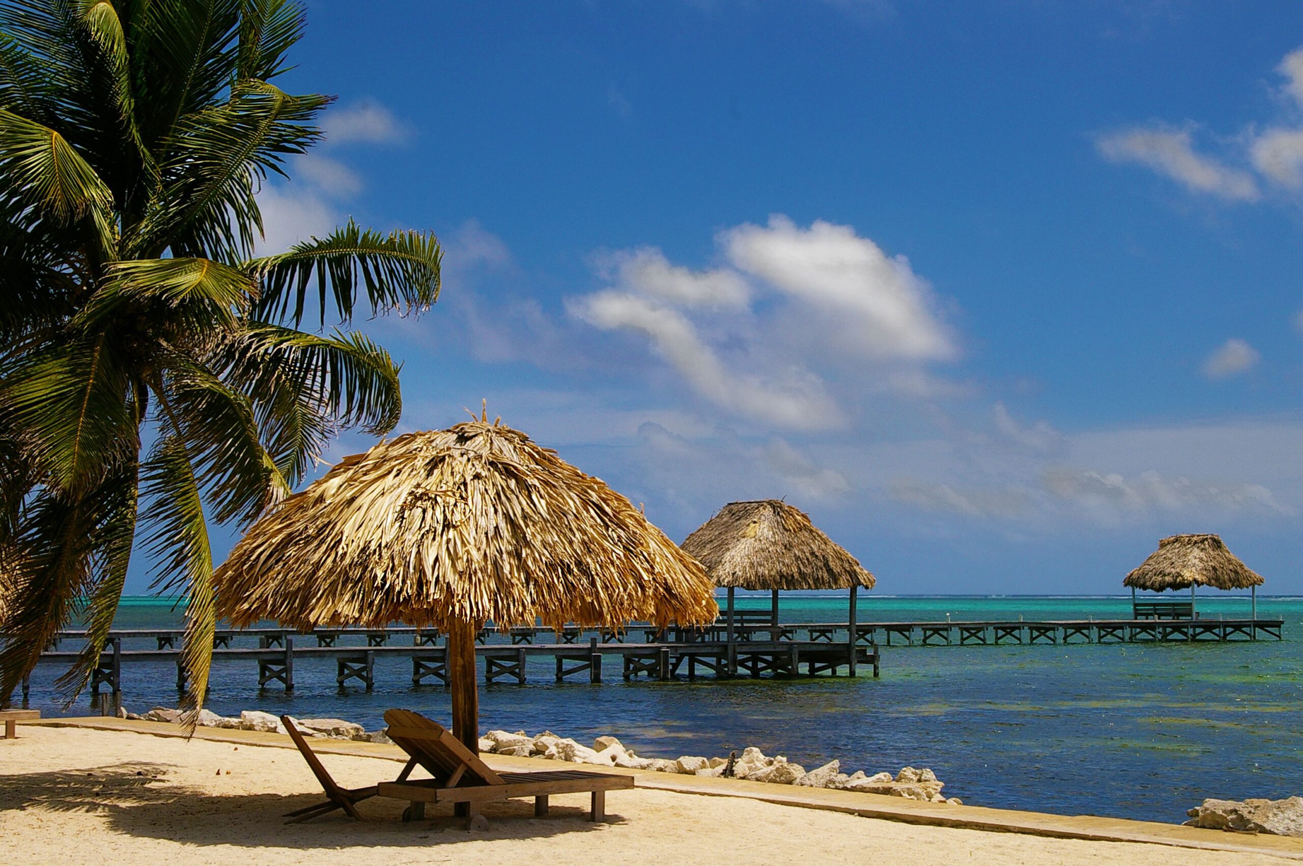 Resort cabana on the beach in Ambergris Caye, Belize with two piers, surrounded by palm trees and ocean in the background on a sunny day