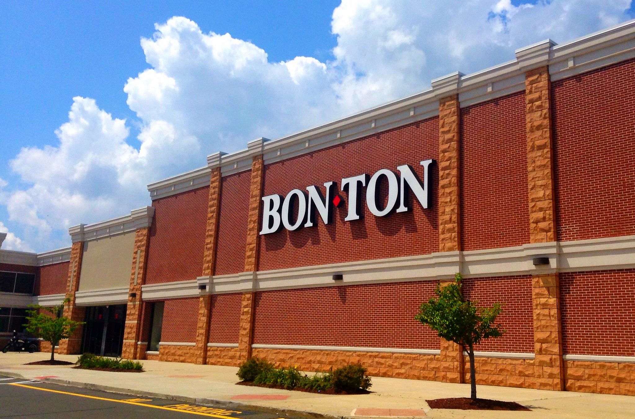 Side exterior of Bon-Ton store, Hamden, Connecticut, red bricks with terracotta brick accents, large sidewalk with green plants, on a sunny day with a blue sky