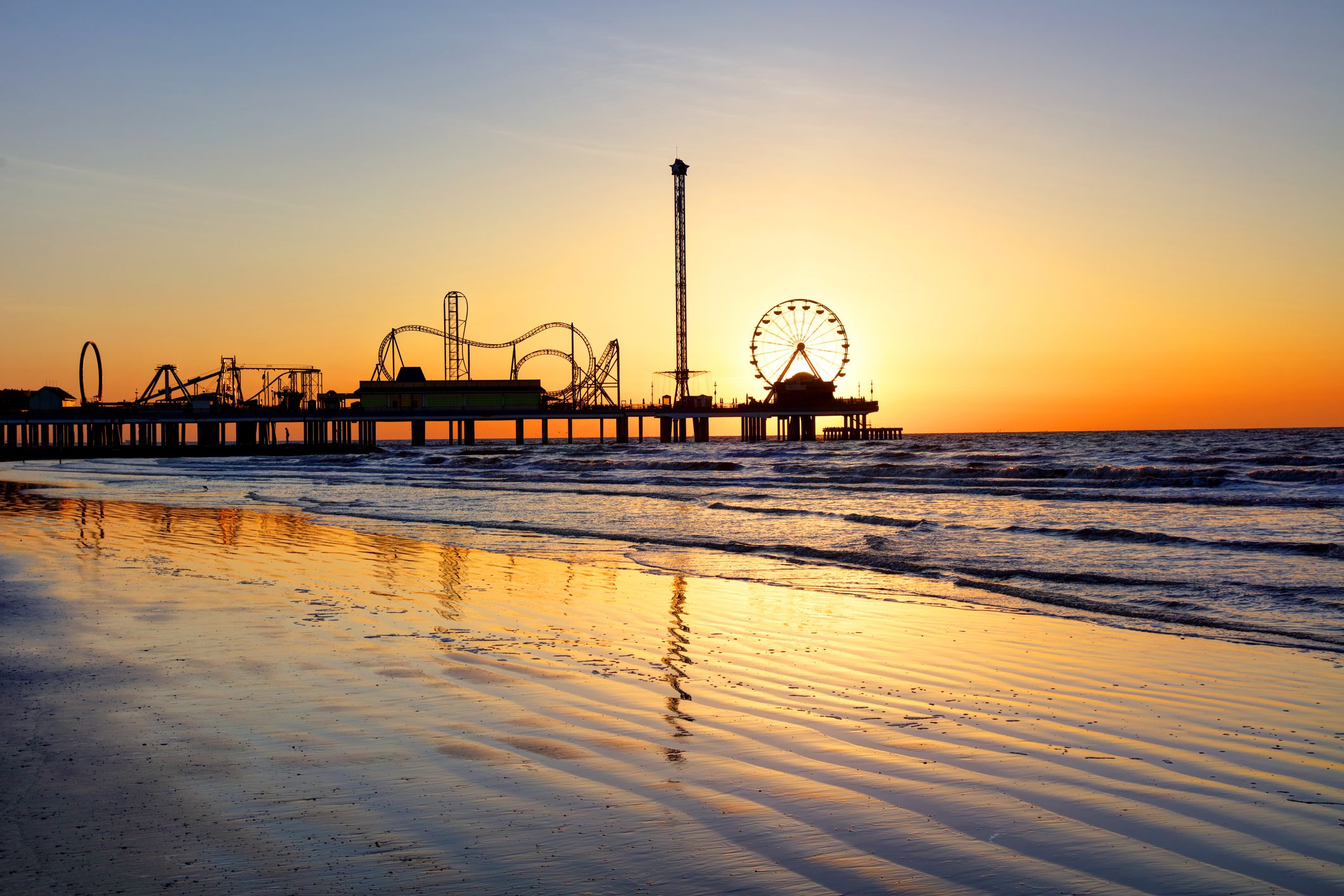 Sunrise showing through Pleasure Pier, Galveston, Texas with beach and ocean