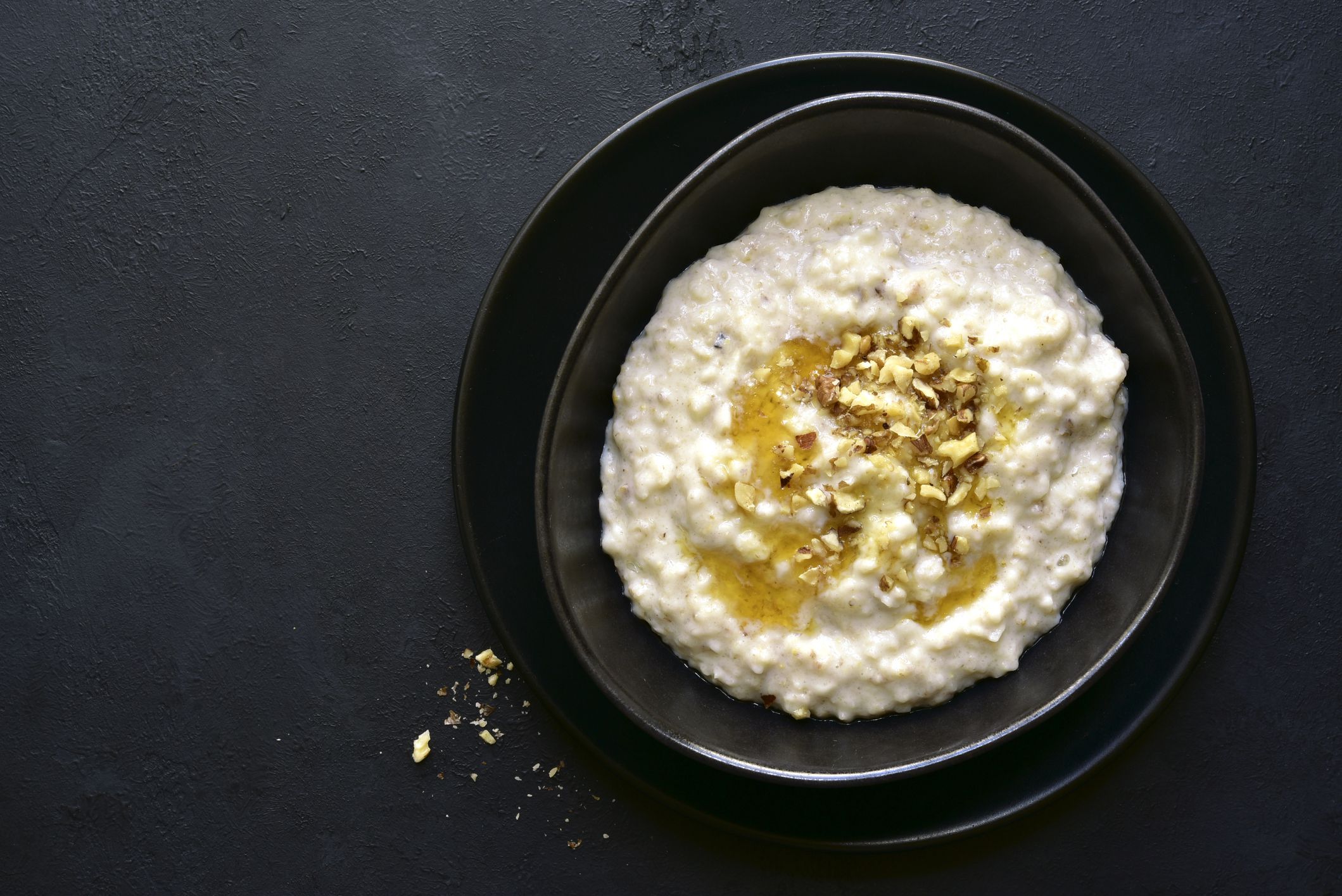 Top view of salted caramel, low-calorie oatmeal in a stack of two black ceramic bowls on a dark grey background with a few crumbs of almonds