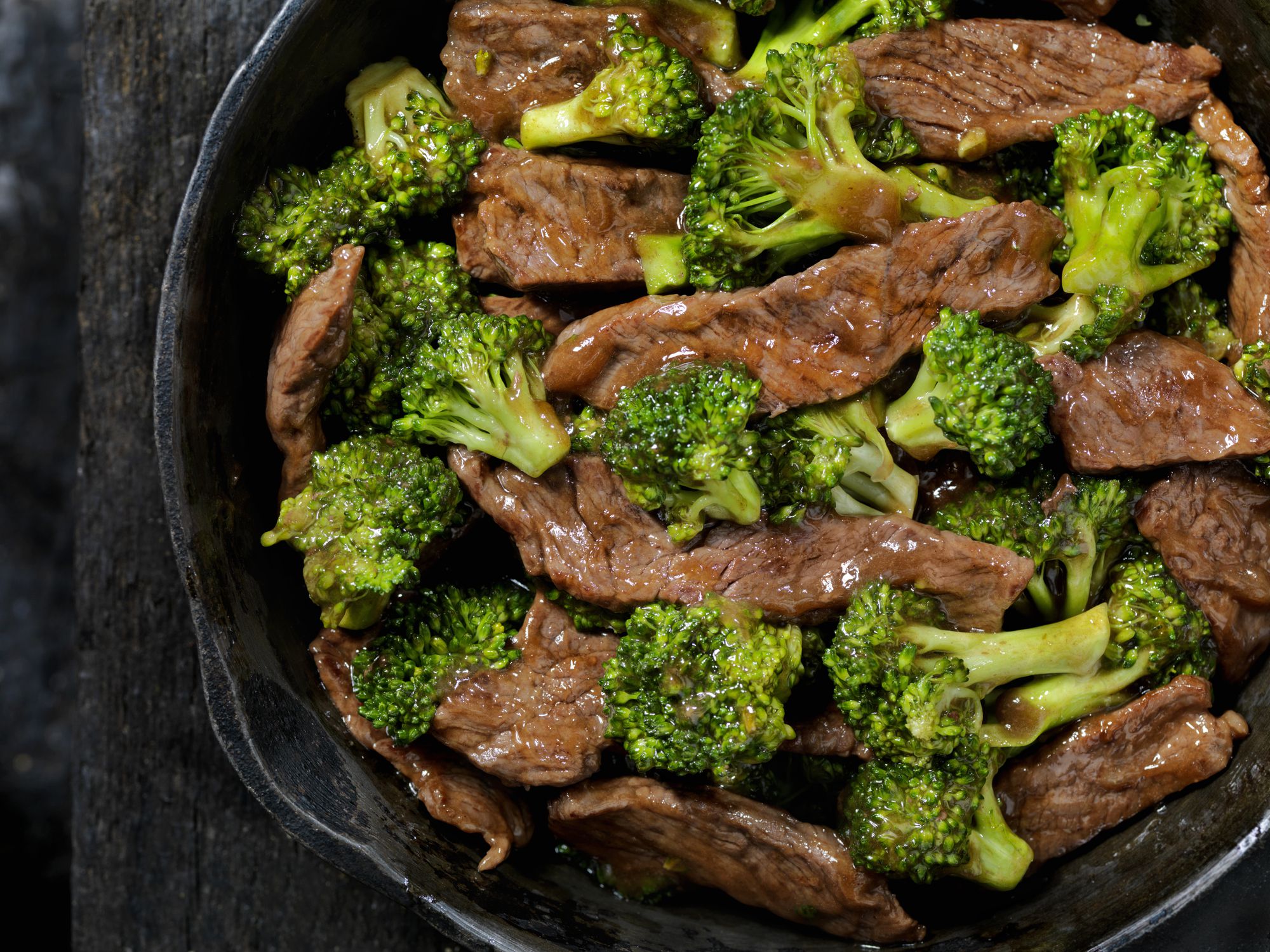 Top view of healthy steak stir-fry in a cast iron skillet on a rustic wooden table with a sliver of the floor showing on the left