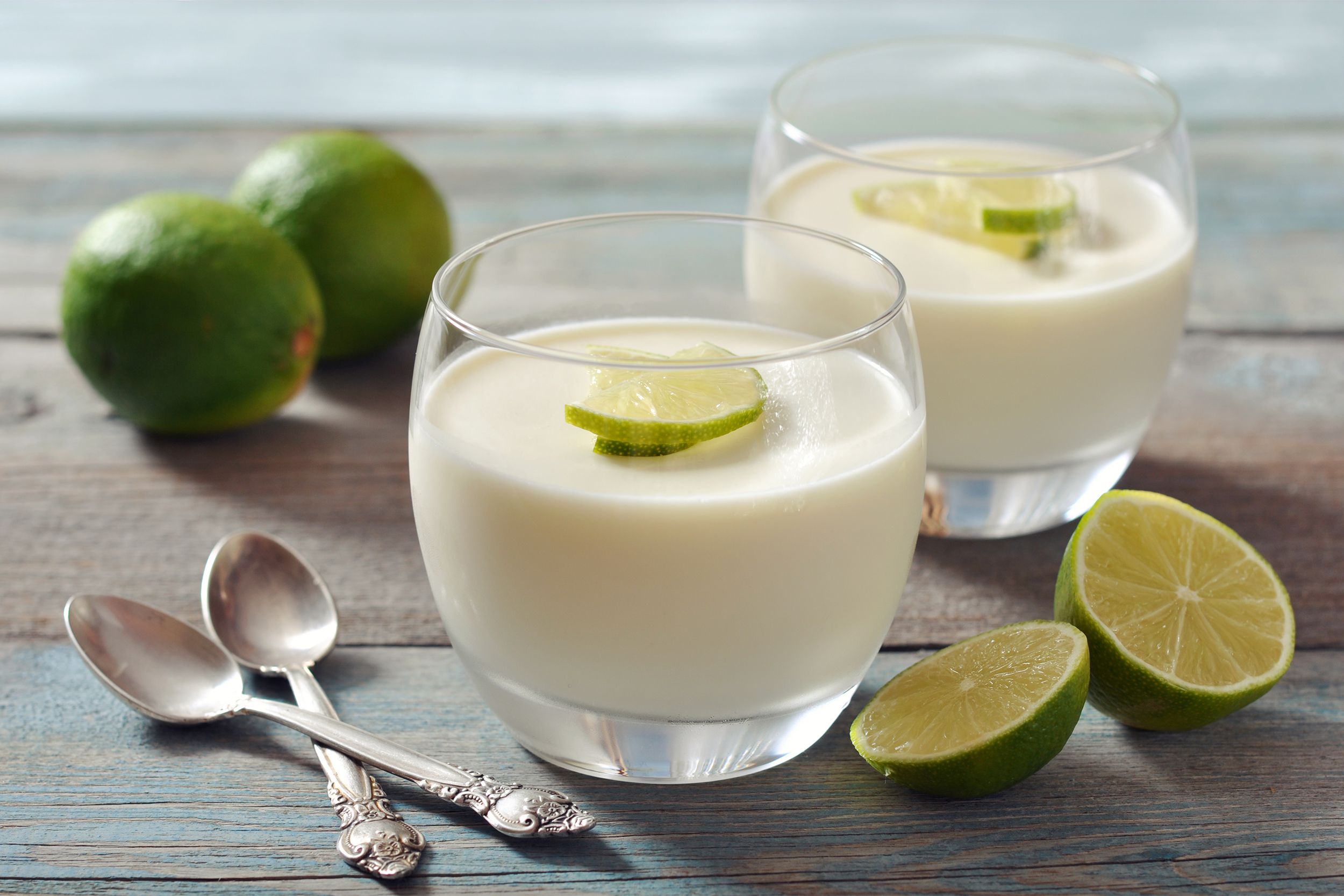 Two dessert glasses of key lime pudding with two spoons and key limes on a wooden table