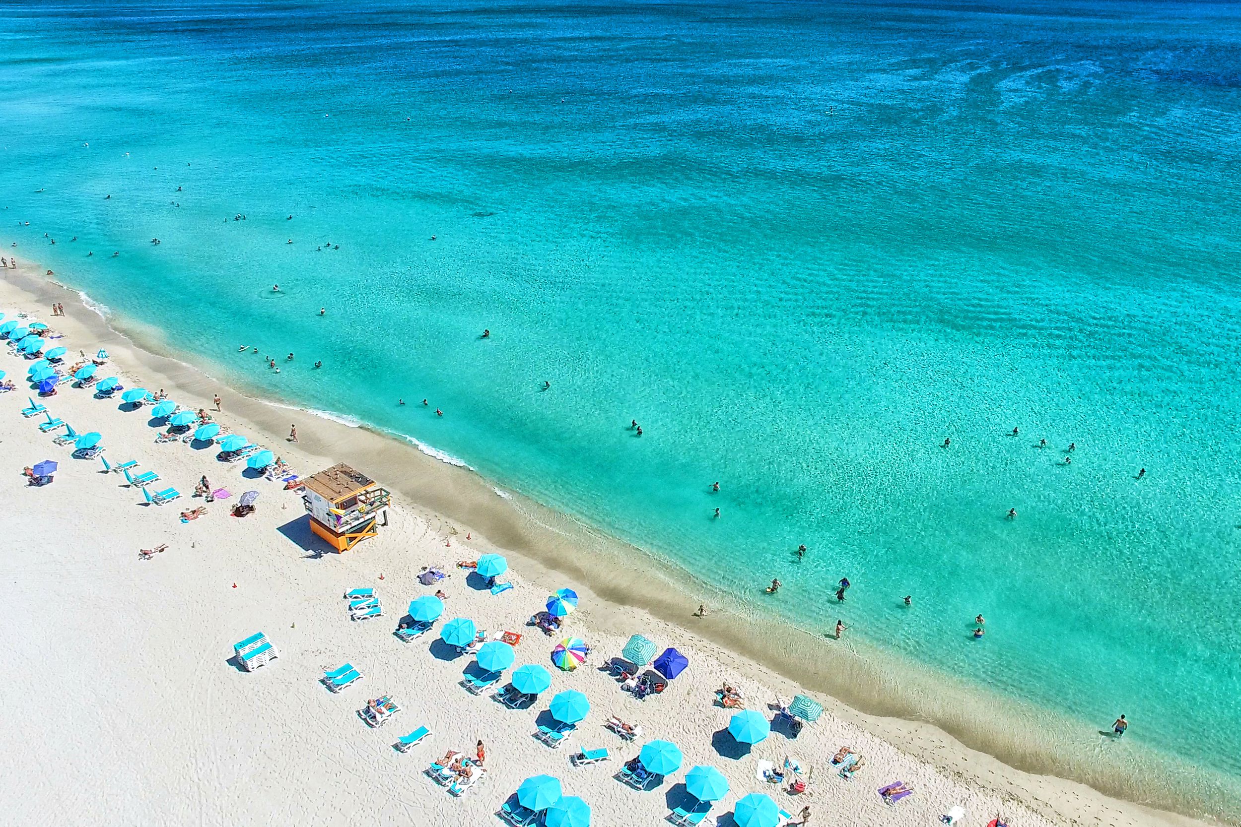 White sand with people and aqua umbrellas and chairs and turquoise ocean in South Beach, Miami, Florida on a sunny day