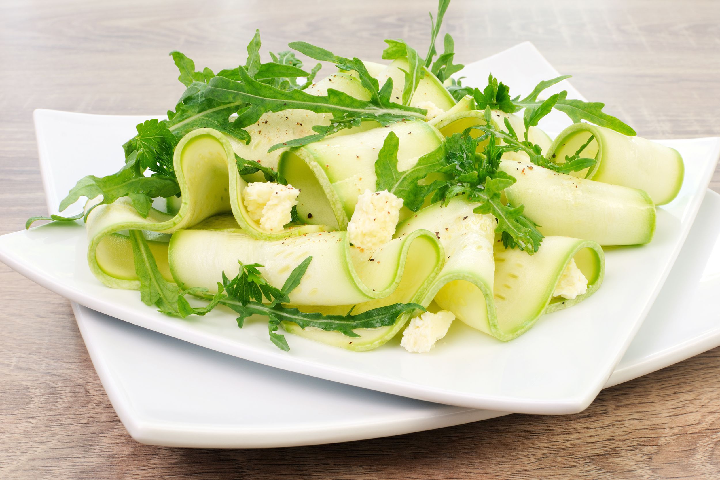 Zucchini ribbon salad on two stacked white square plates on a wooden table