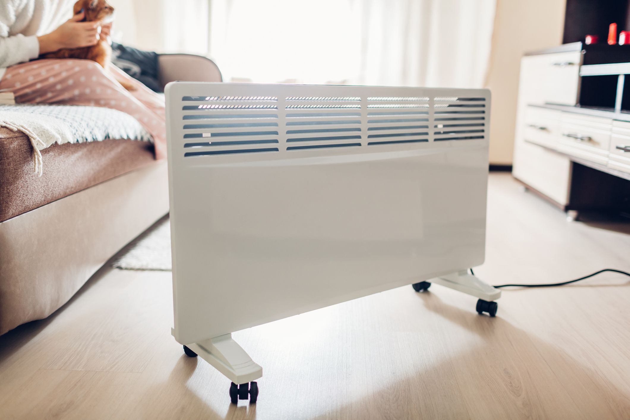 Using heater at home in winter. Woman warming during playing with her cat sitting by device. Heating season.