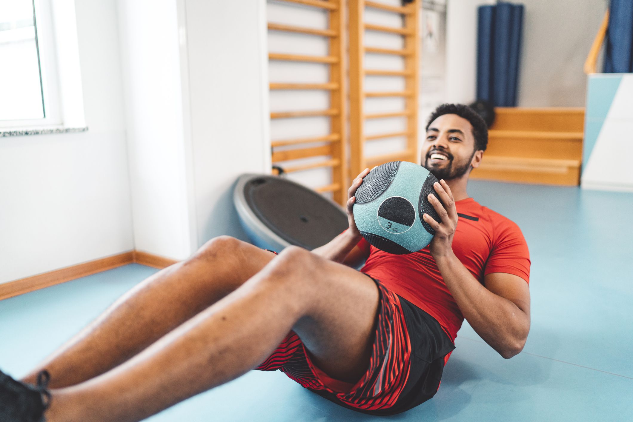 Afroamerican man doing side abs exercise with a medicine ball at the gym.