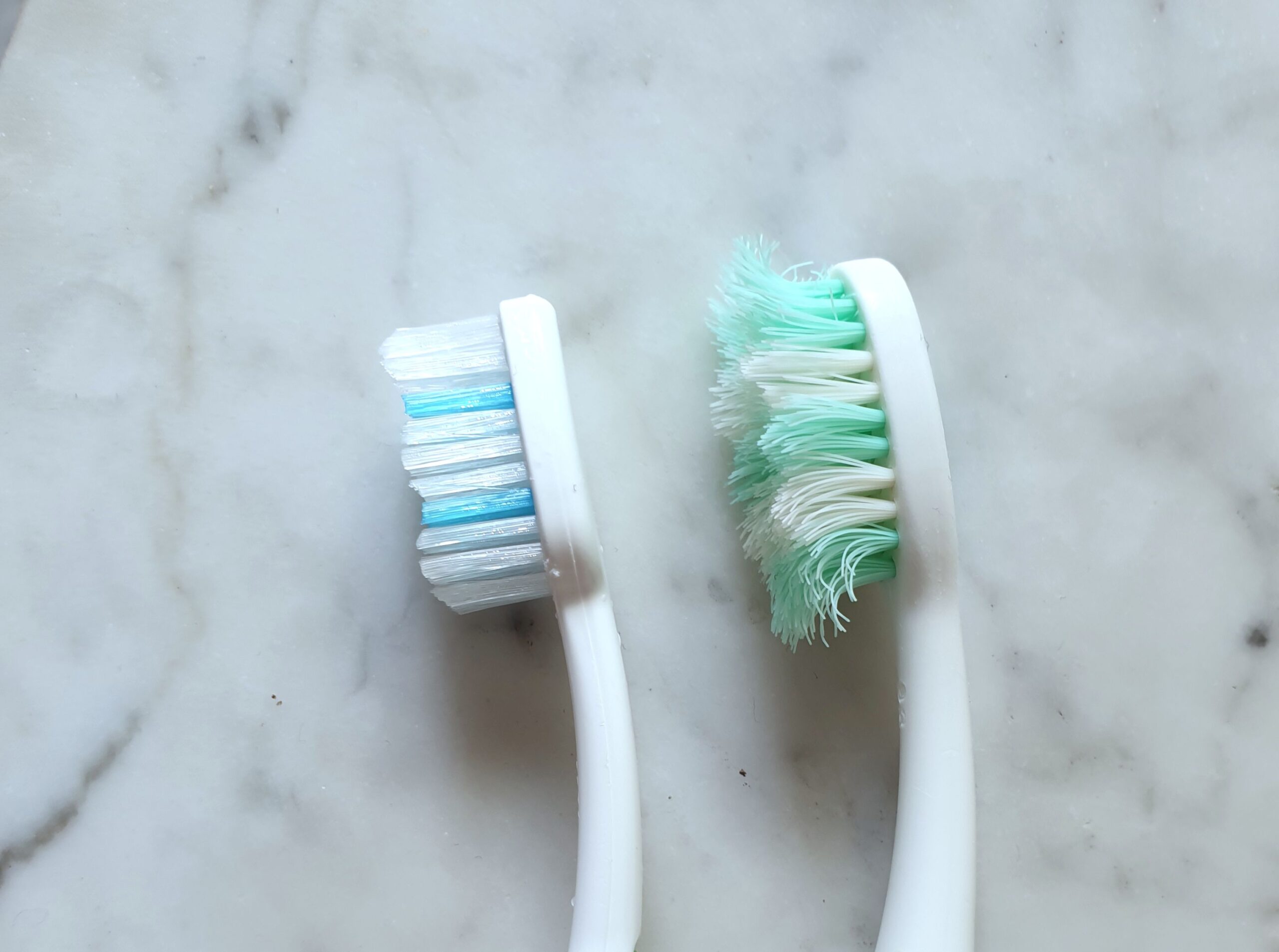 Two plastic toothbrushes, with white and green bristles One used and one brand new. Minimalist image with marble textured background. Scene with natural light. Top view.