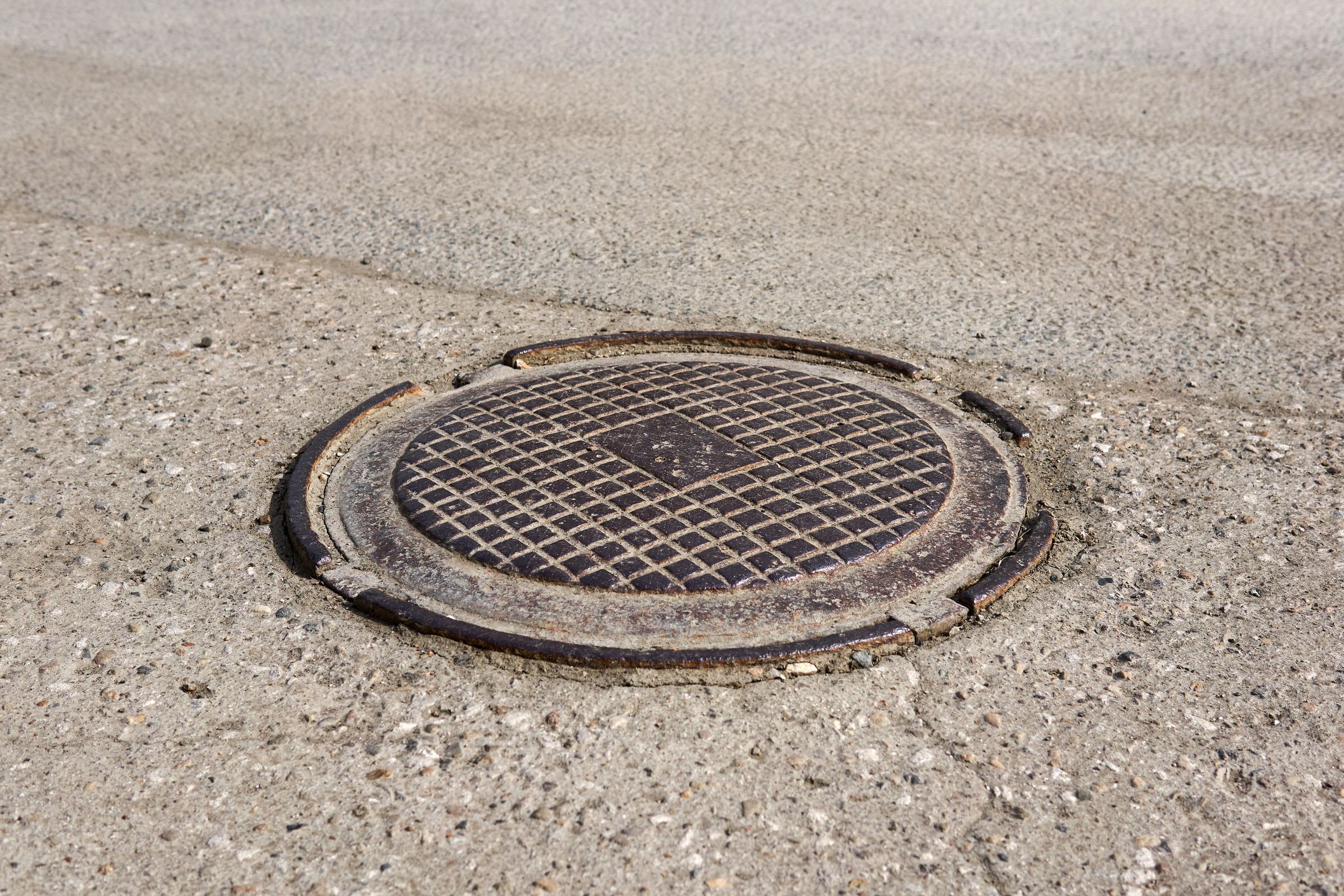 old shabby metal manhole cover in dusty asphalt