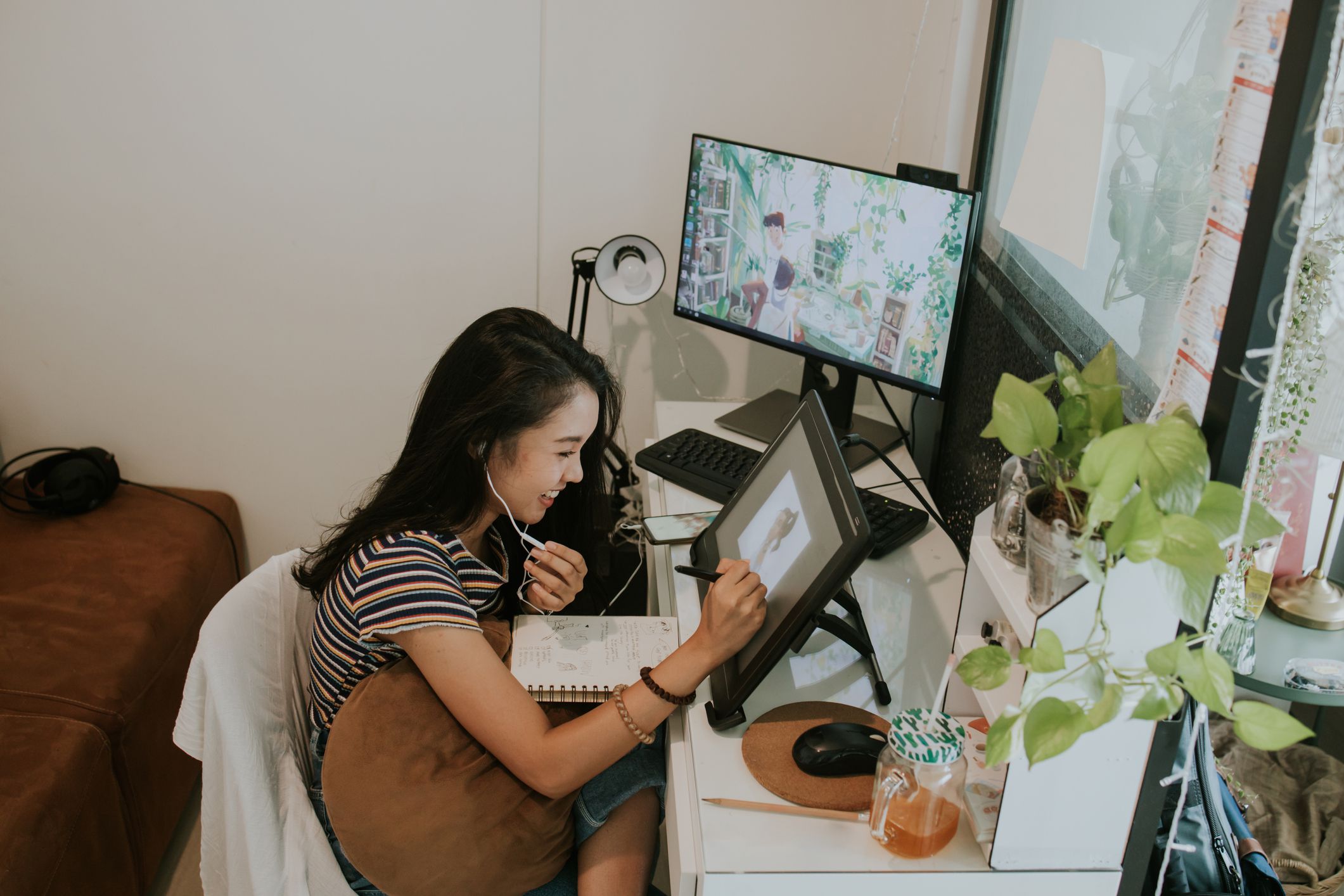 Thai young animator creator discussing her work with client in the smartphone while sketching her cartoon character at her small office space, Bangkok Thailand