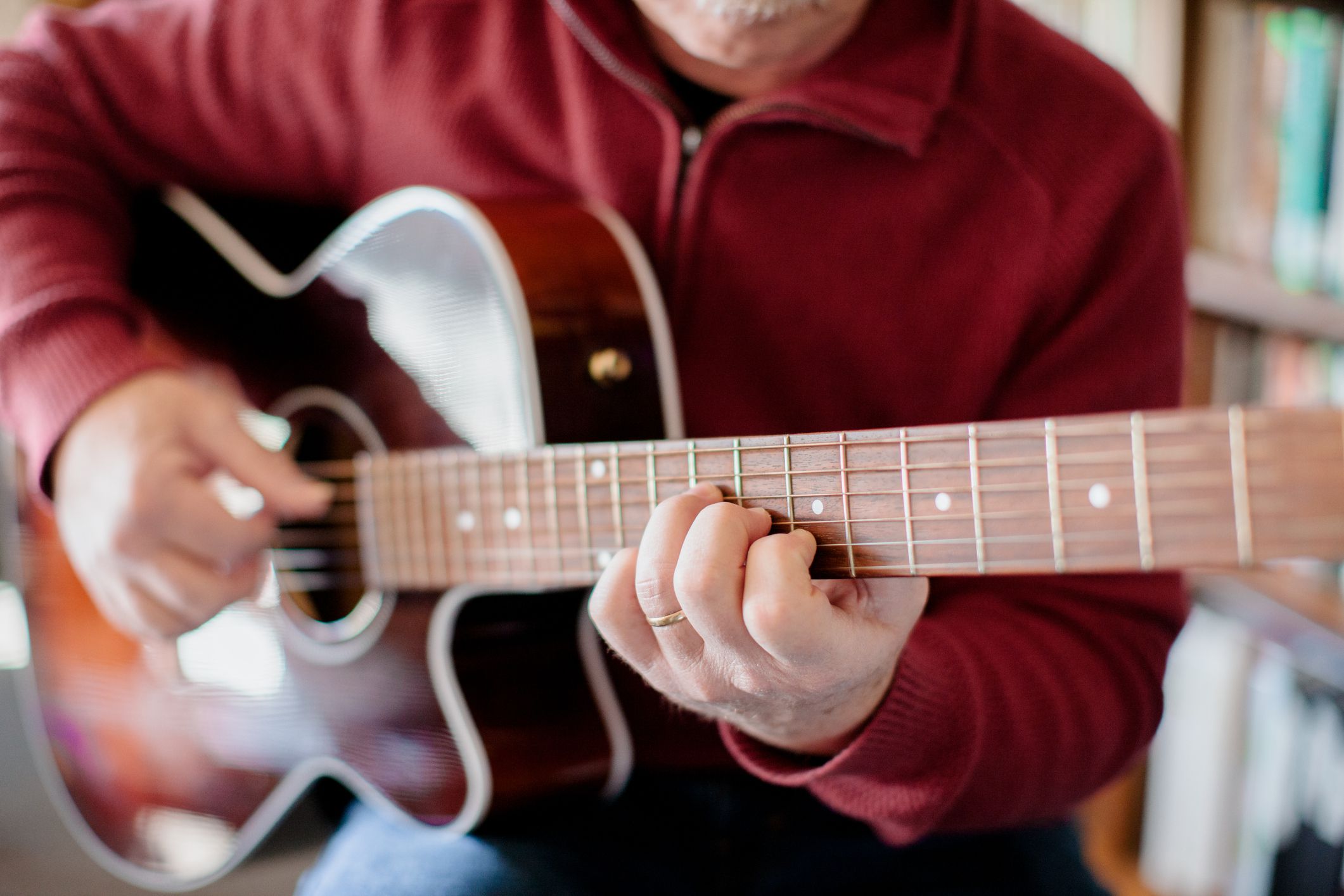 Lifestyle portraits of a middle aged man, about 55 years, playing guitar in his personal study/library. He is wearing a red sweater and has glasses and a mustache, all natural light used.