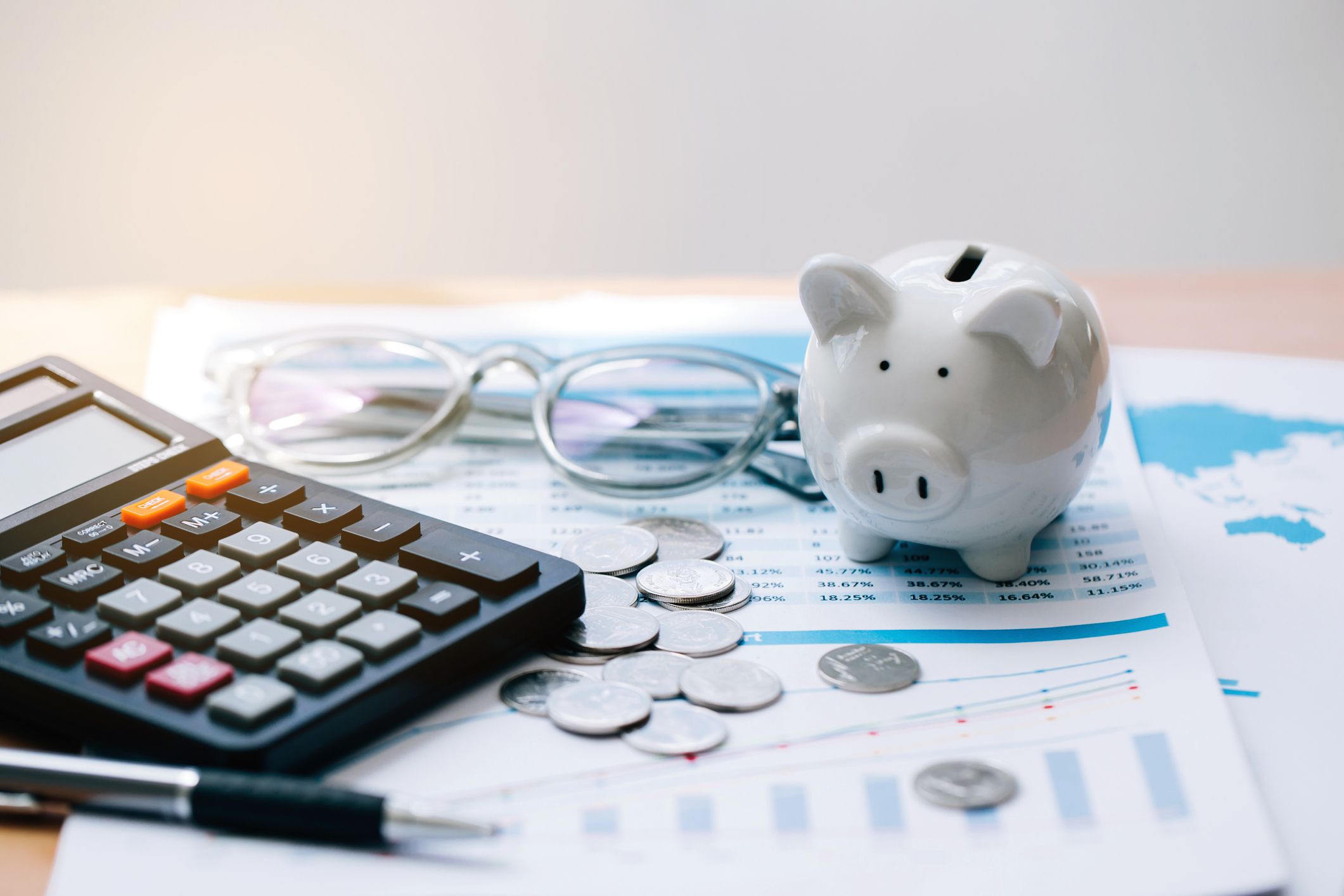 Calculator with text Tax Saving. Calculator, Piggy Bank, coins, business graph and pen on wooden table.