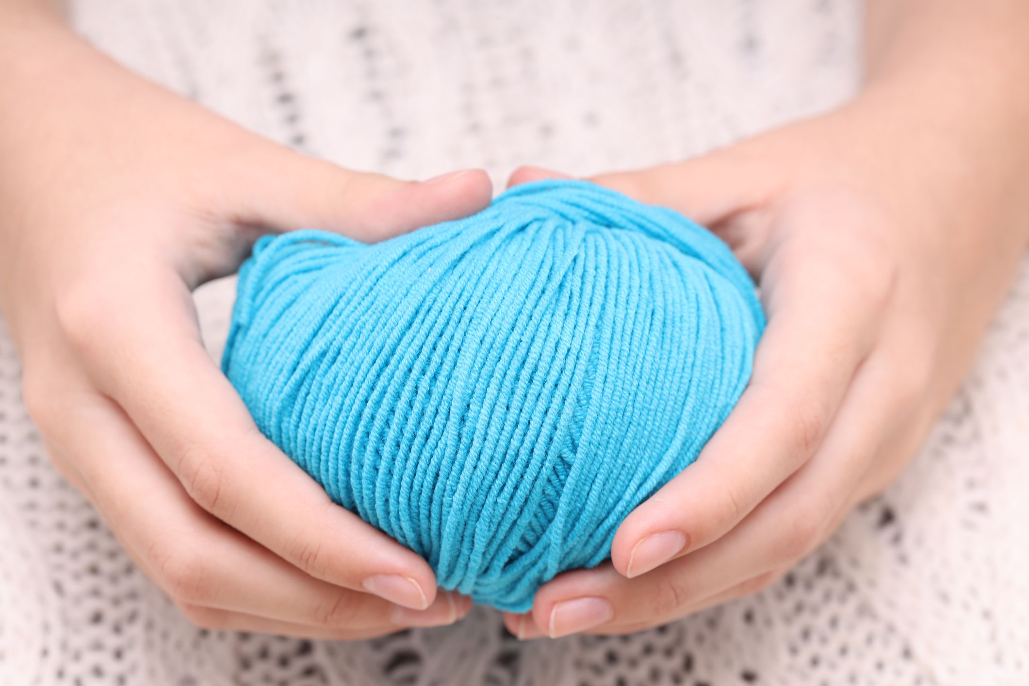 blue ball of wool in hands on the background of a white knitted tablecloth. High quality photo
