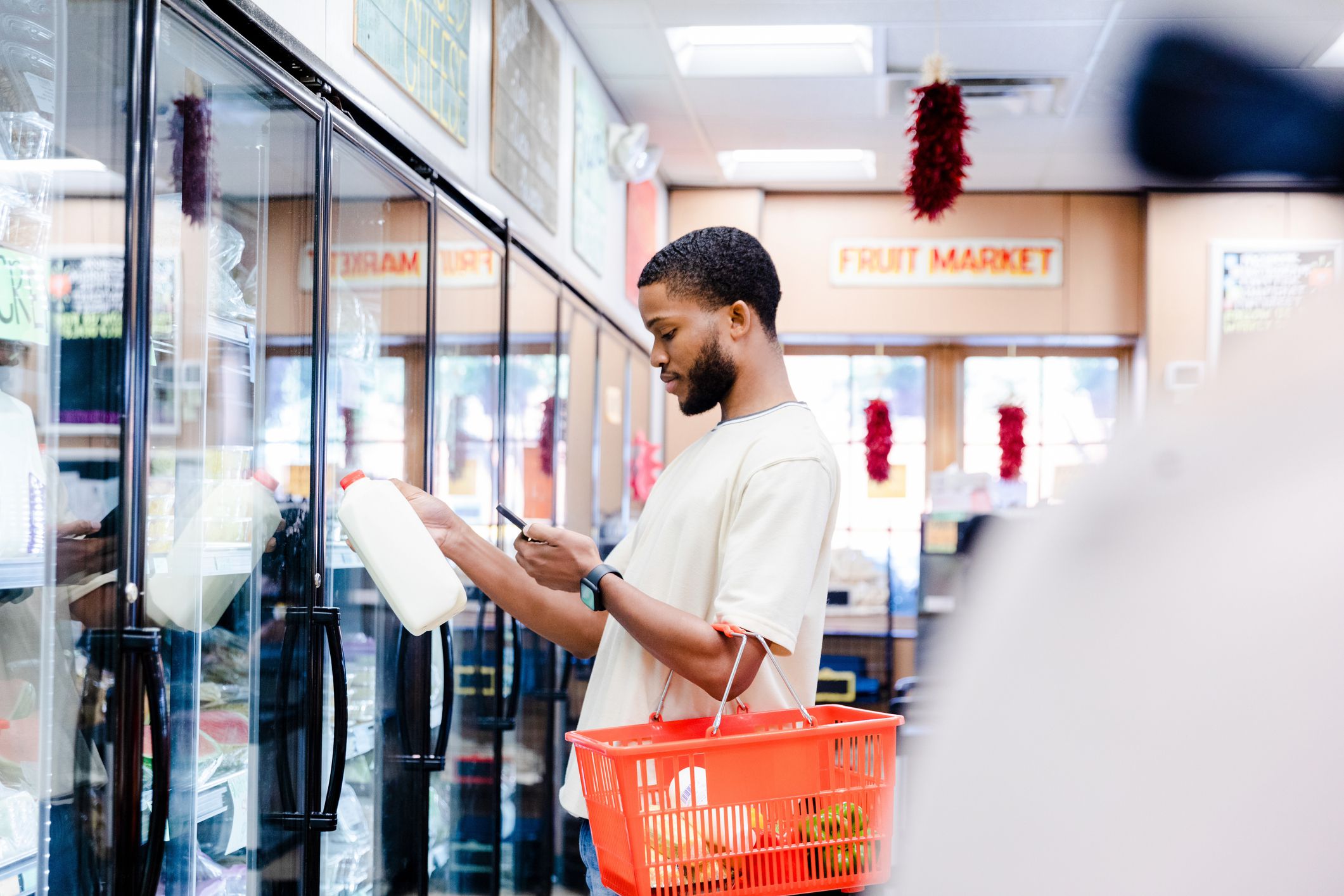 The young adult male reads a message from his friend about needing more items from the grocery store while he is shopping.