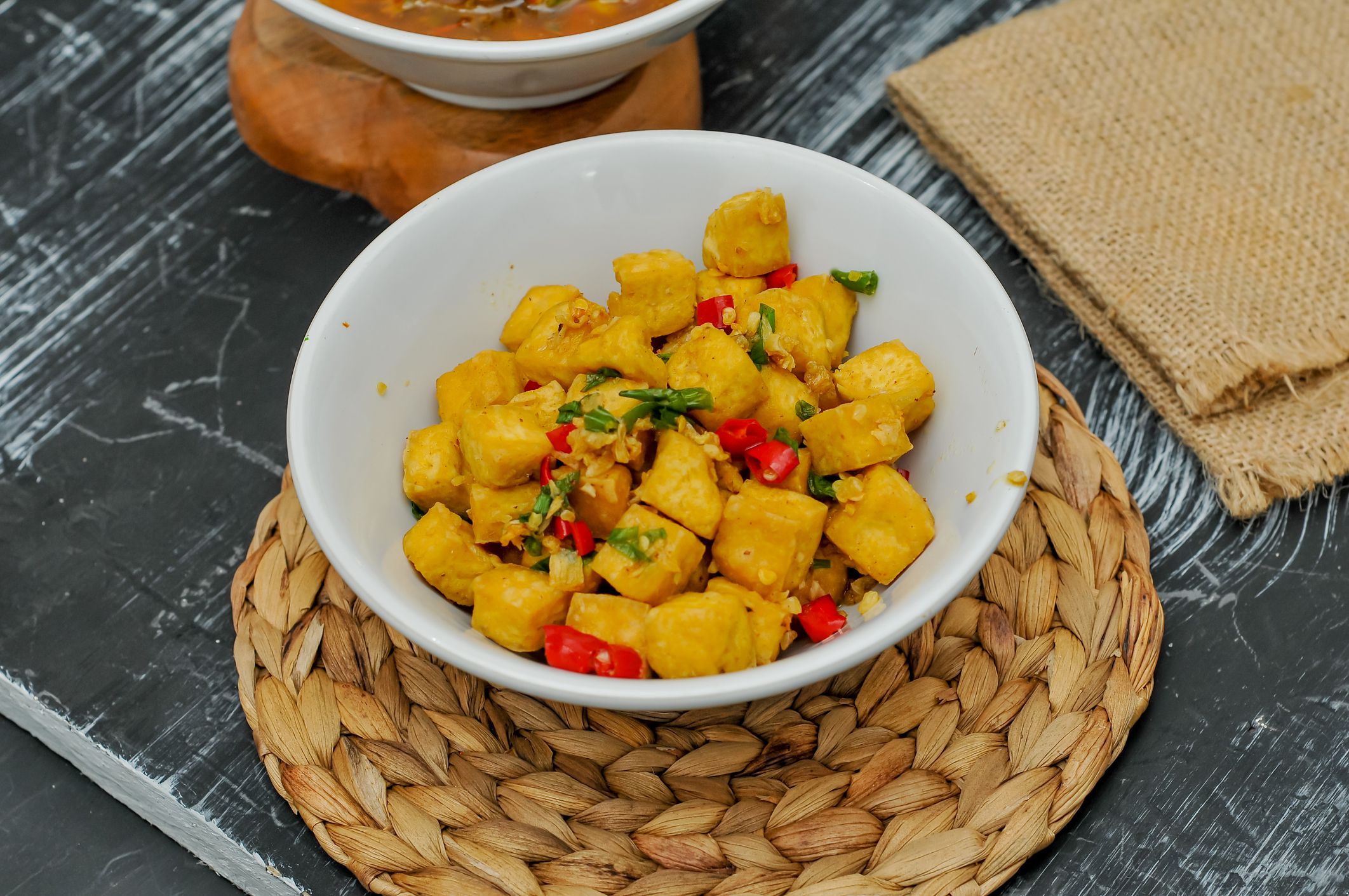 Pepper-fried tofu in a white bowl and on a wooden mat