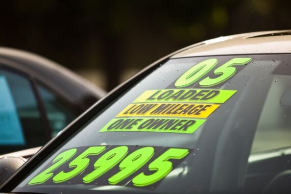 Car windshield featuring neon green and yellow stickers that read “05,” “LOADED,” “LOW MILEAGE,” “ONE OWNER,” and “25995.”