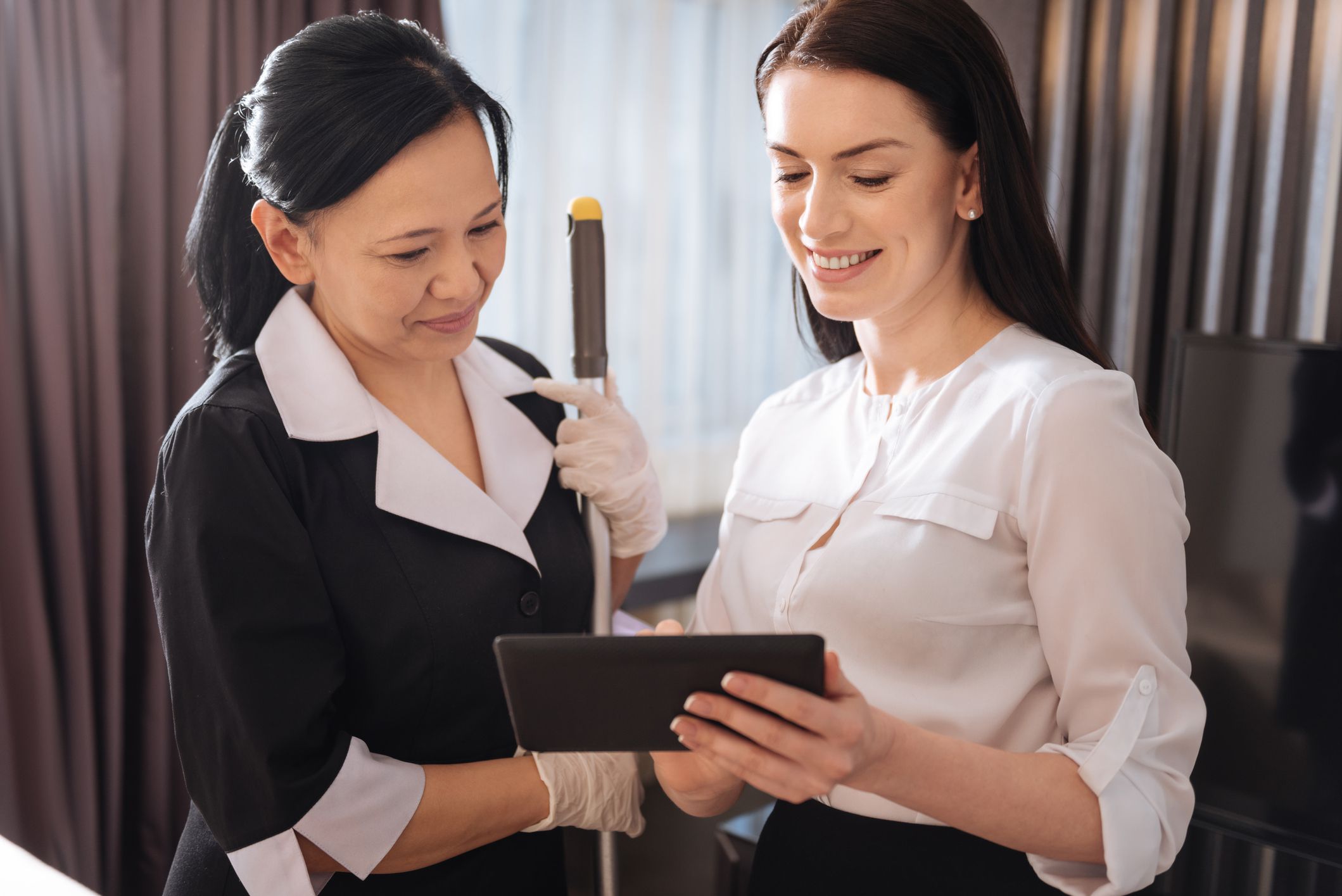 Pleasant communication. Joyful pleasant nice woman standing together and looking at the tablet screen while discussing work issues