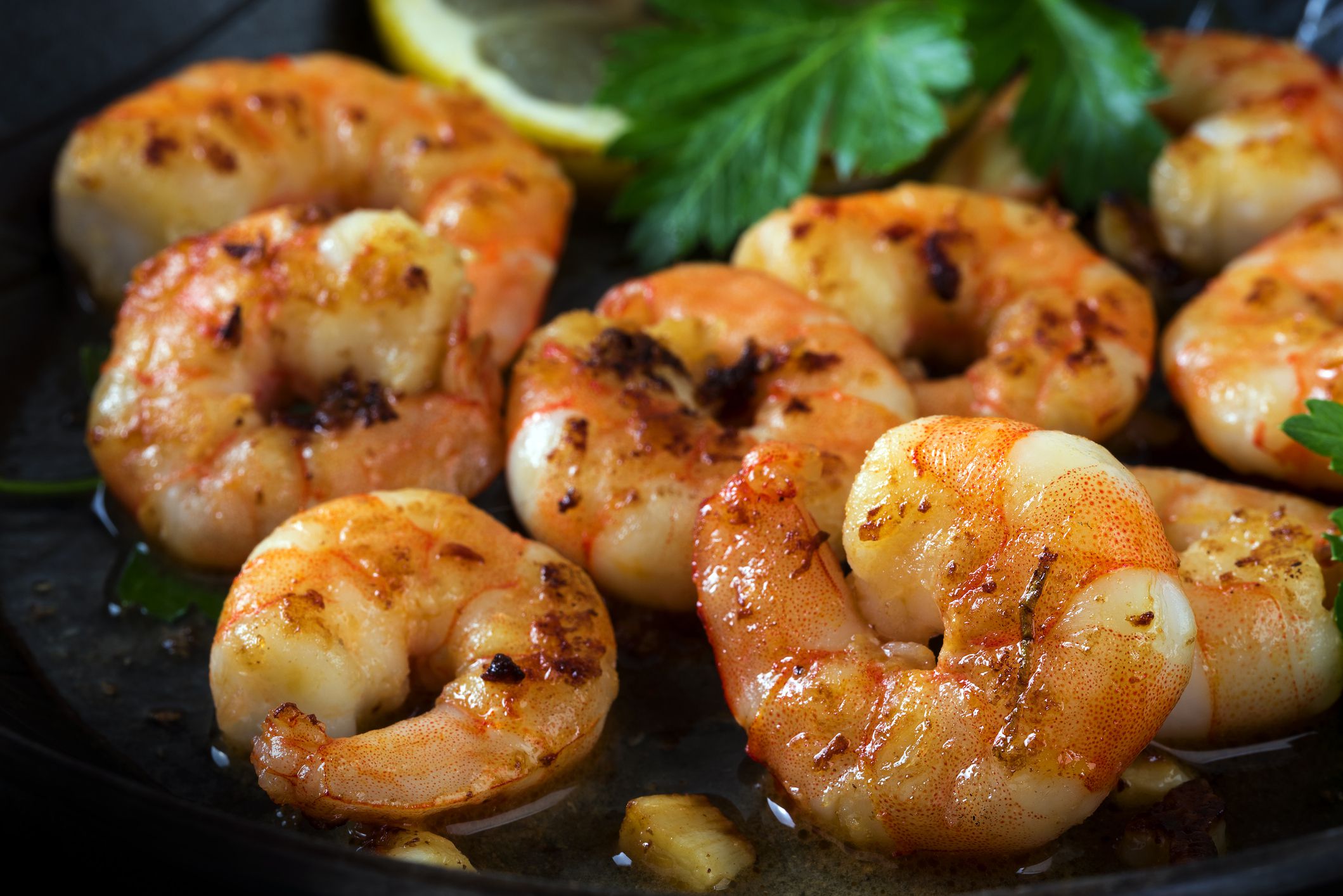 prawns shrimps roasted in a black pan with garlic, lemon, spices and italian parsley garnish, close up, selected focus, narrow depth of field