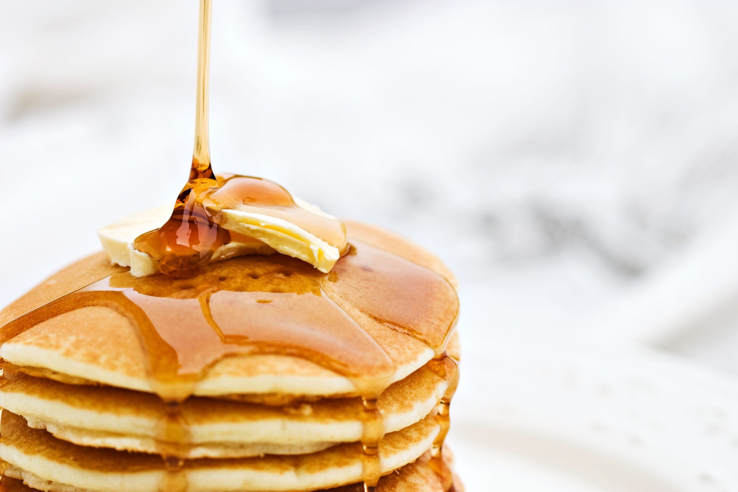 Maple syrup pouring onto pancakes. Shallow DOF with focus on syrup and butter.