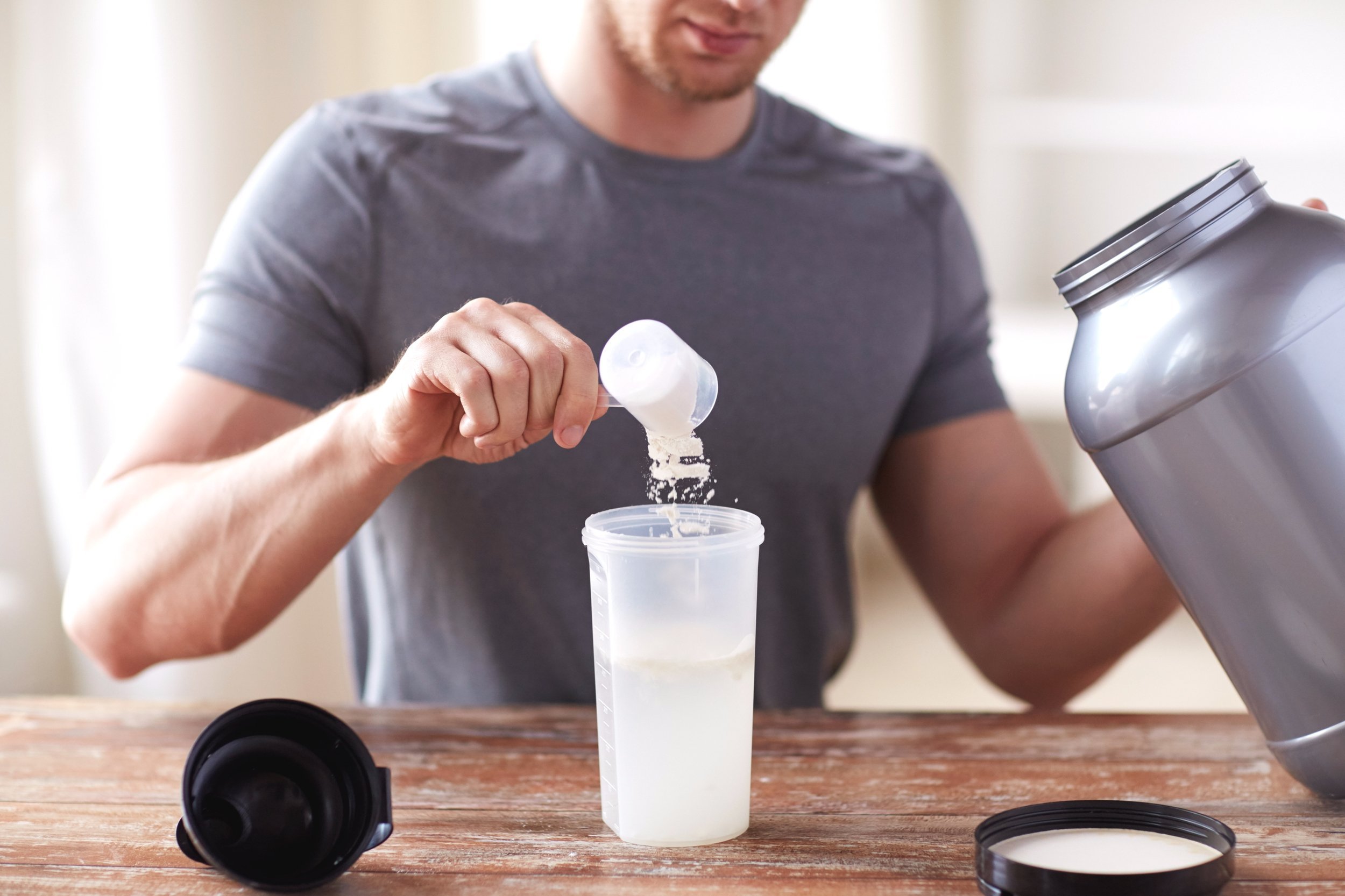 Close up of man with jar and bottle preparing protein shake.